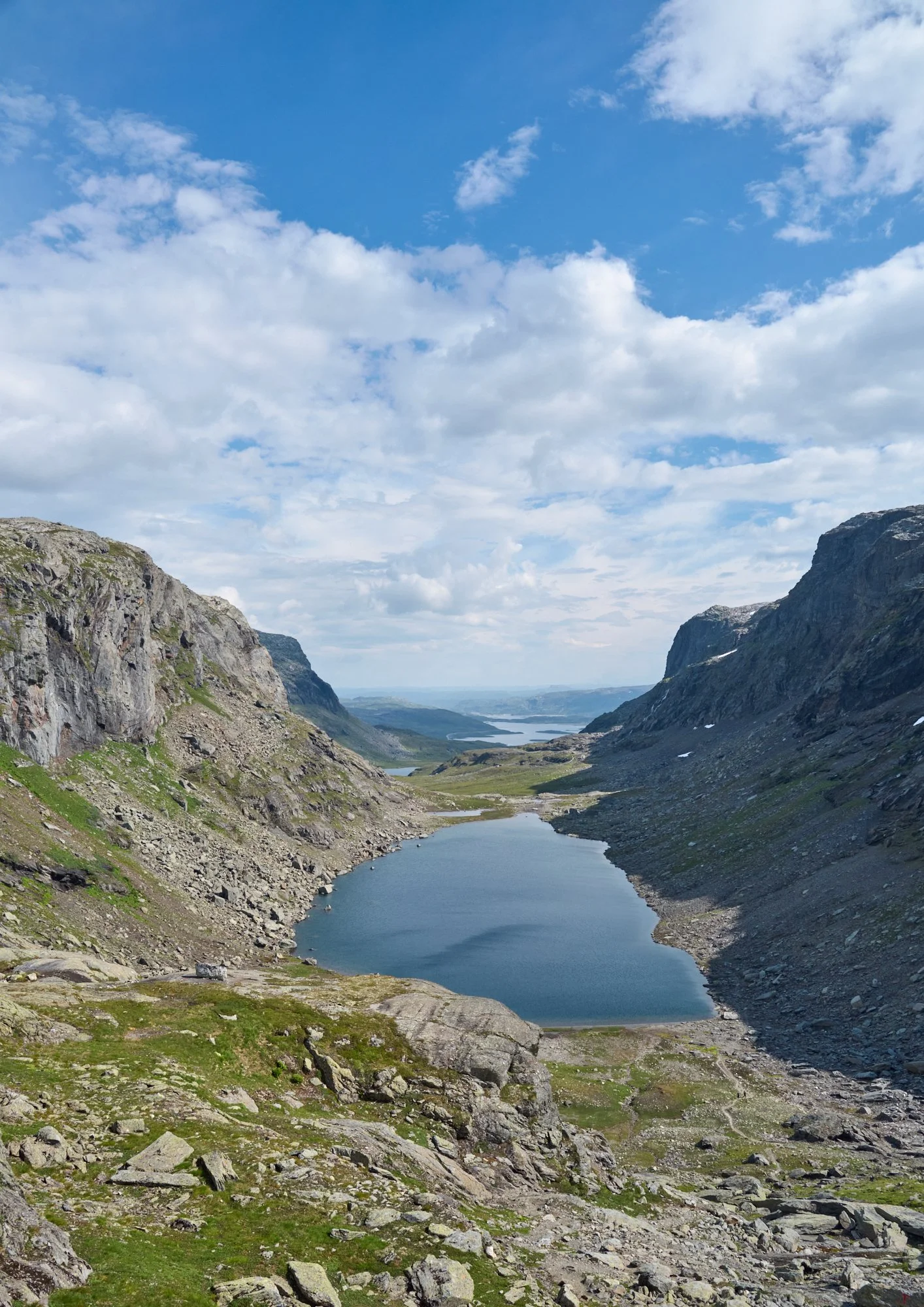 Scenic a mountainous landscape with a valley and a lake, surrounded by cliffs and a partly cloudy sky.