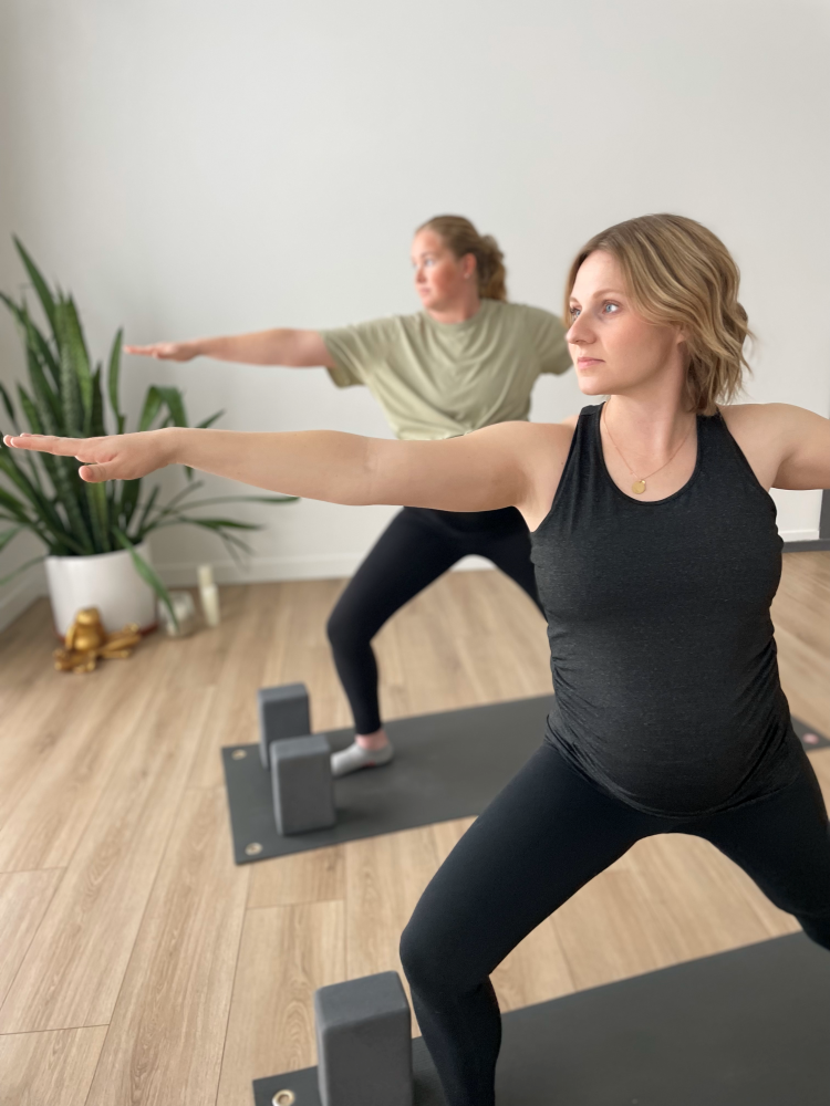 Two pregnant women practicing Warrior II yoga pose.