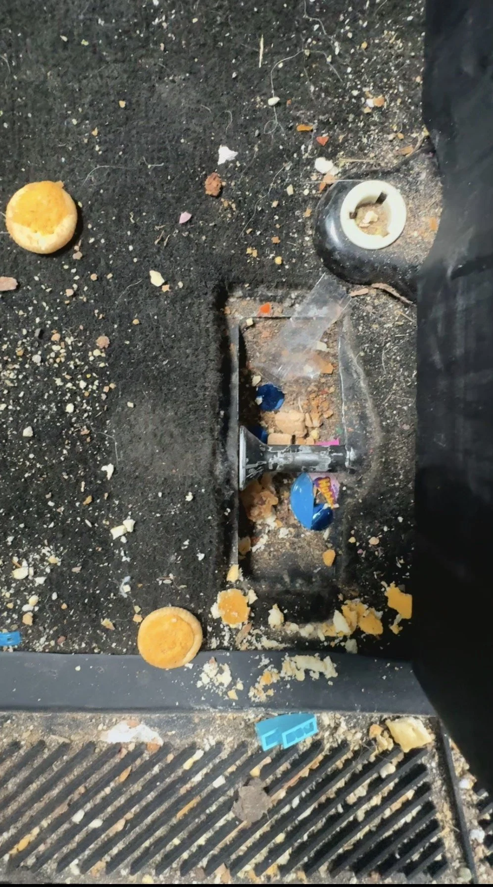 Dirty car floor with spilled crumbs, broken potato chips, scattered trash, a USB drive, and an exposed screw.