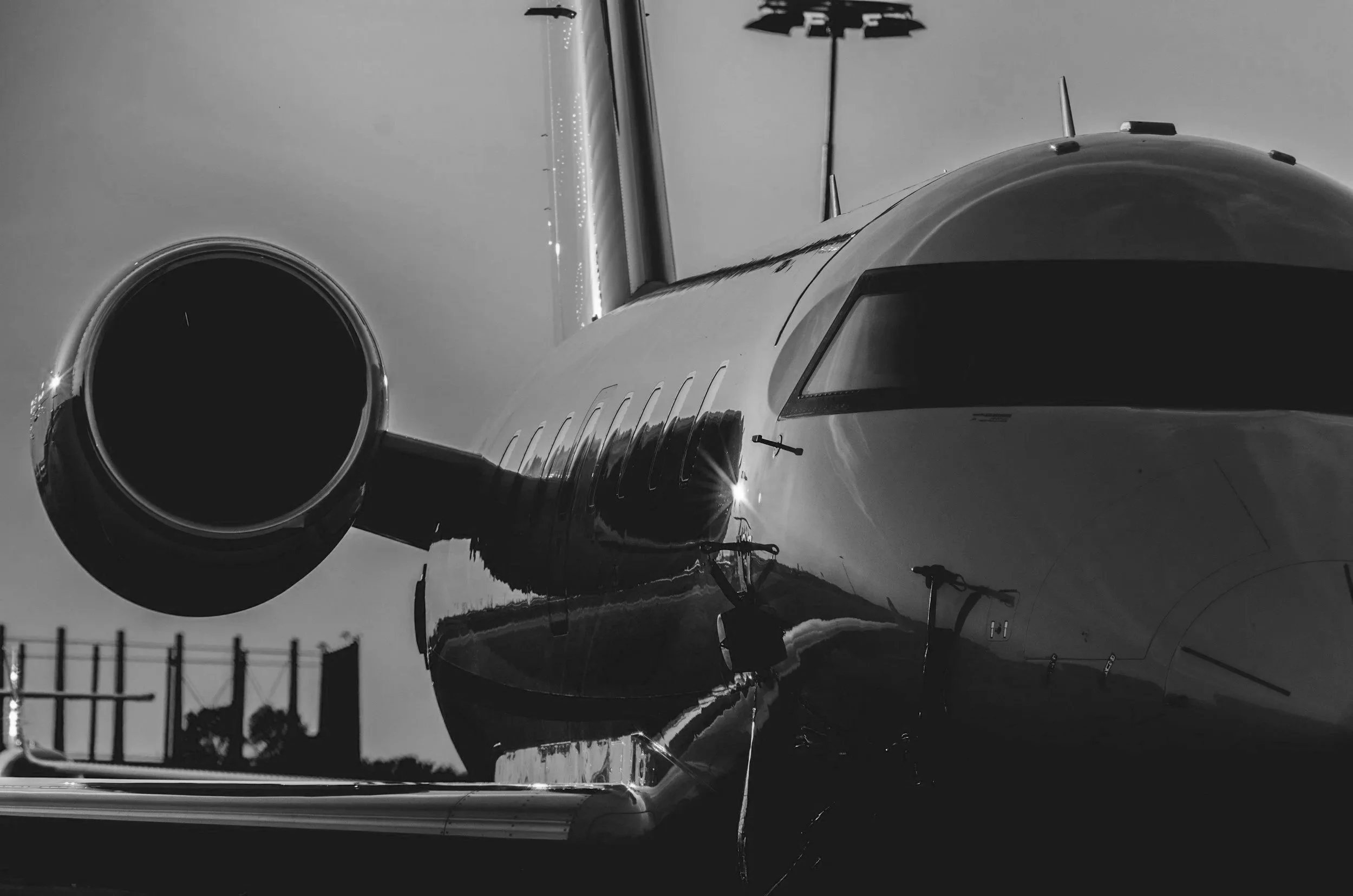 Black and white photo of a private jet airplane parked on the tarmac, with a clear sky and some structures in the background.