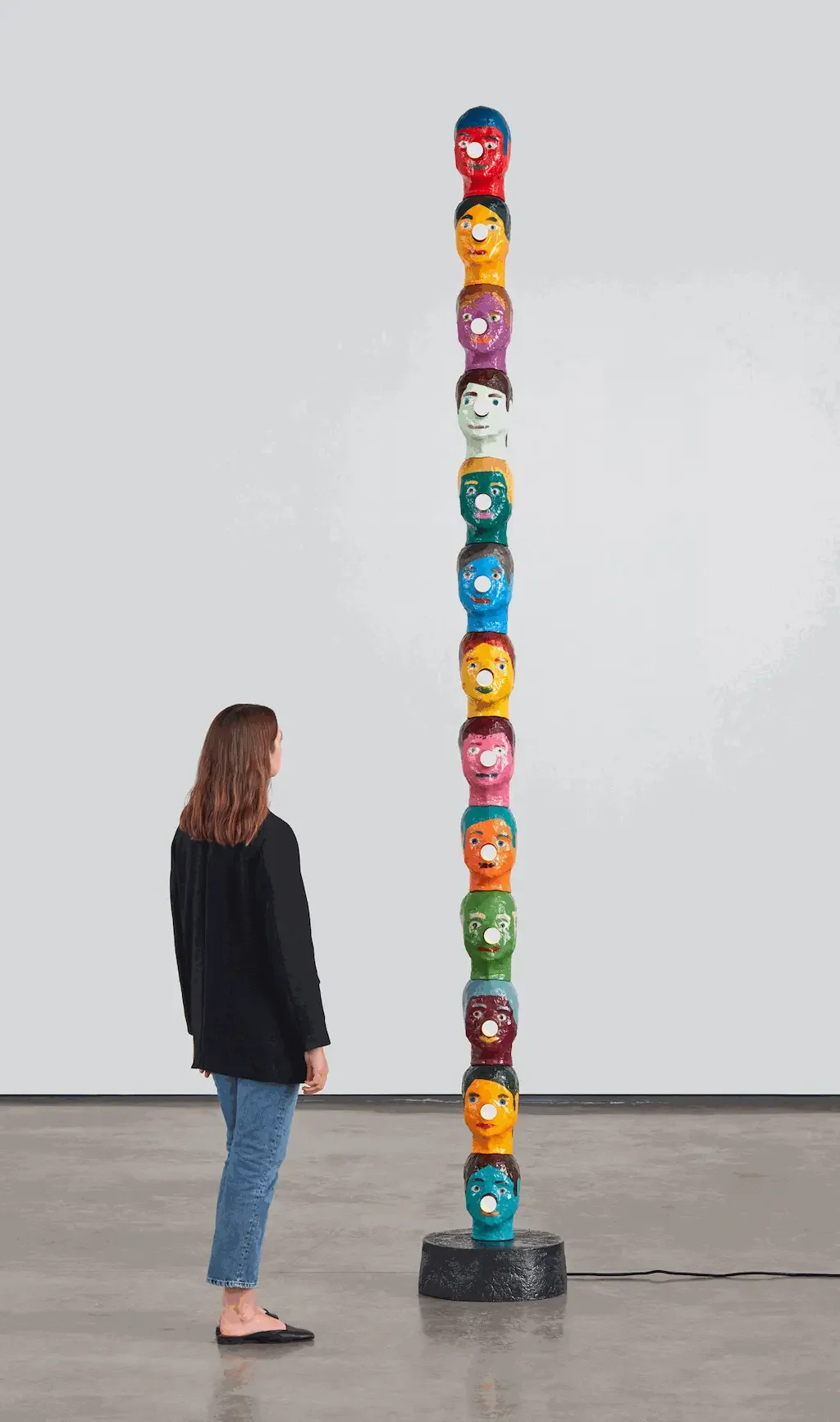 Person looking at a sculpture of colorful stacked heads.