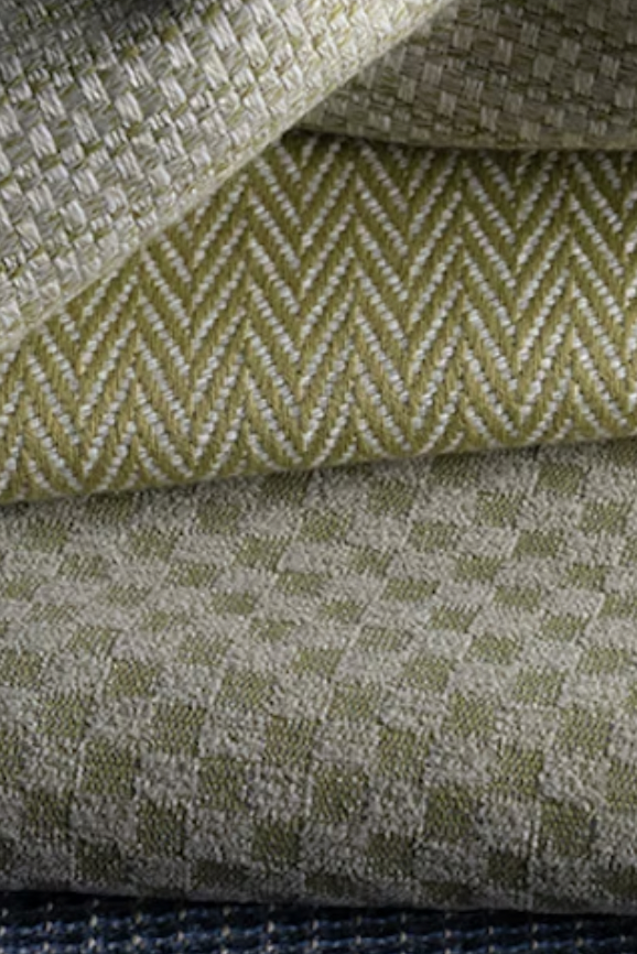 Close-up view of three folded textured fabric pieces with geometric woven patterns in shades of yellow and gray.