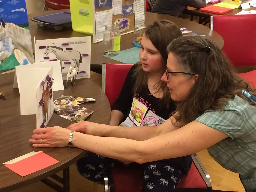 Une femme et une jeune fille regardent des photos et des figurines d'animaux sur une table lors d'une activité éducative.