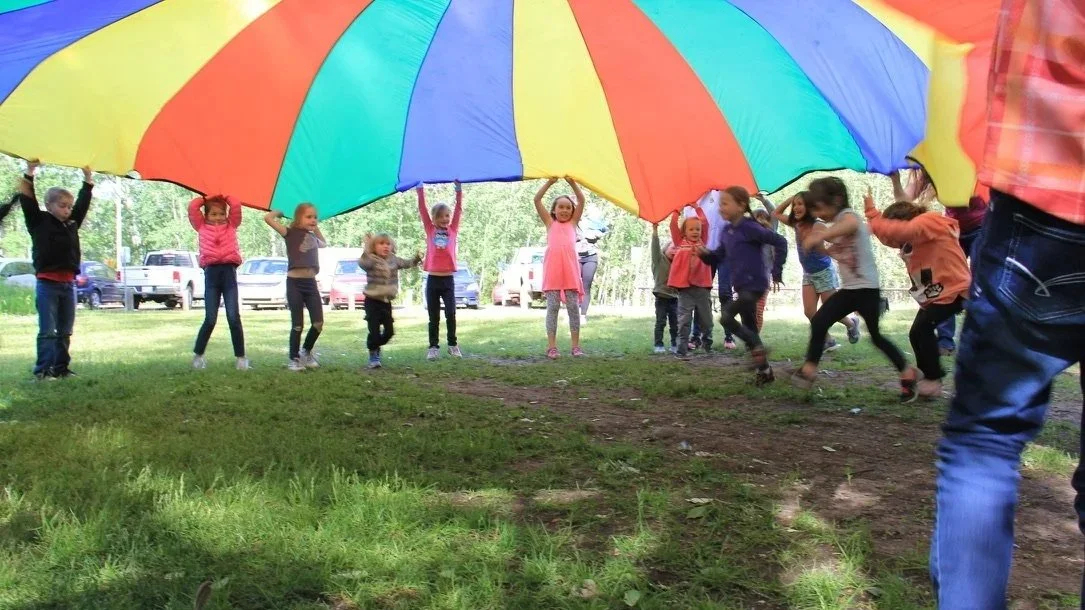 Des enfants jouent sous un grand parachute coloré dans un parc.