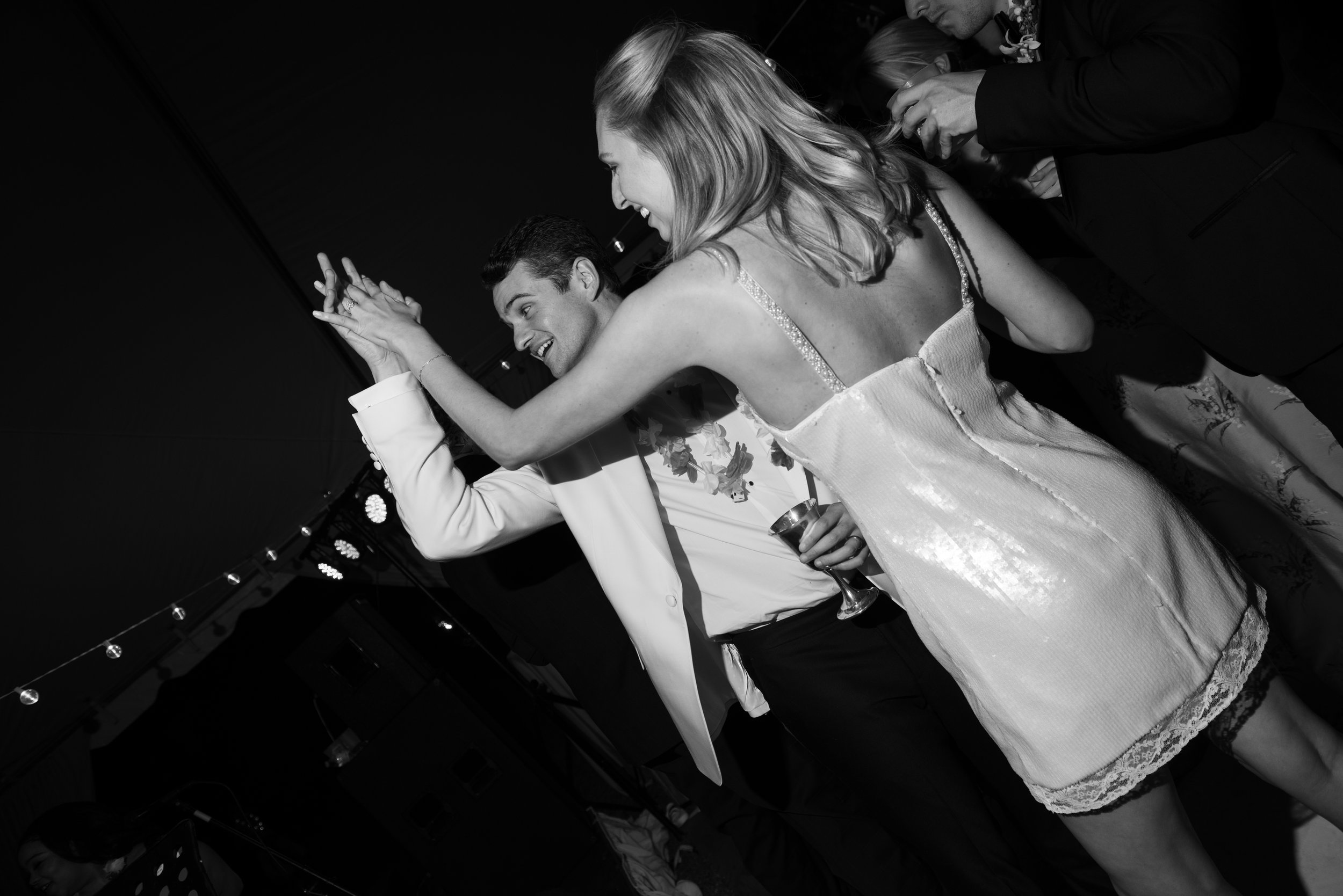 Black and white photo of a young man and woman dancing together at a celebration, smiling and holding hands.