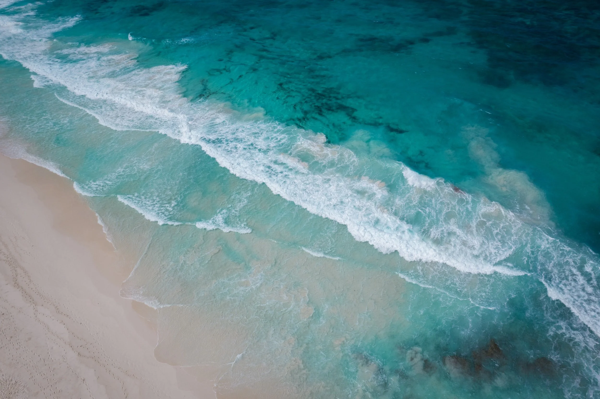 Aerial view of ocean waves crashing on a sandy beach with turquoise water.