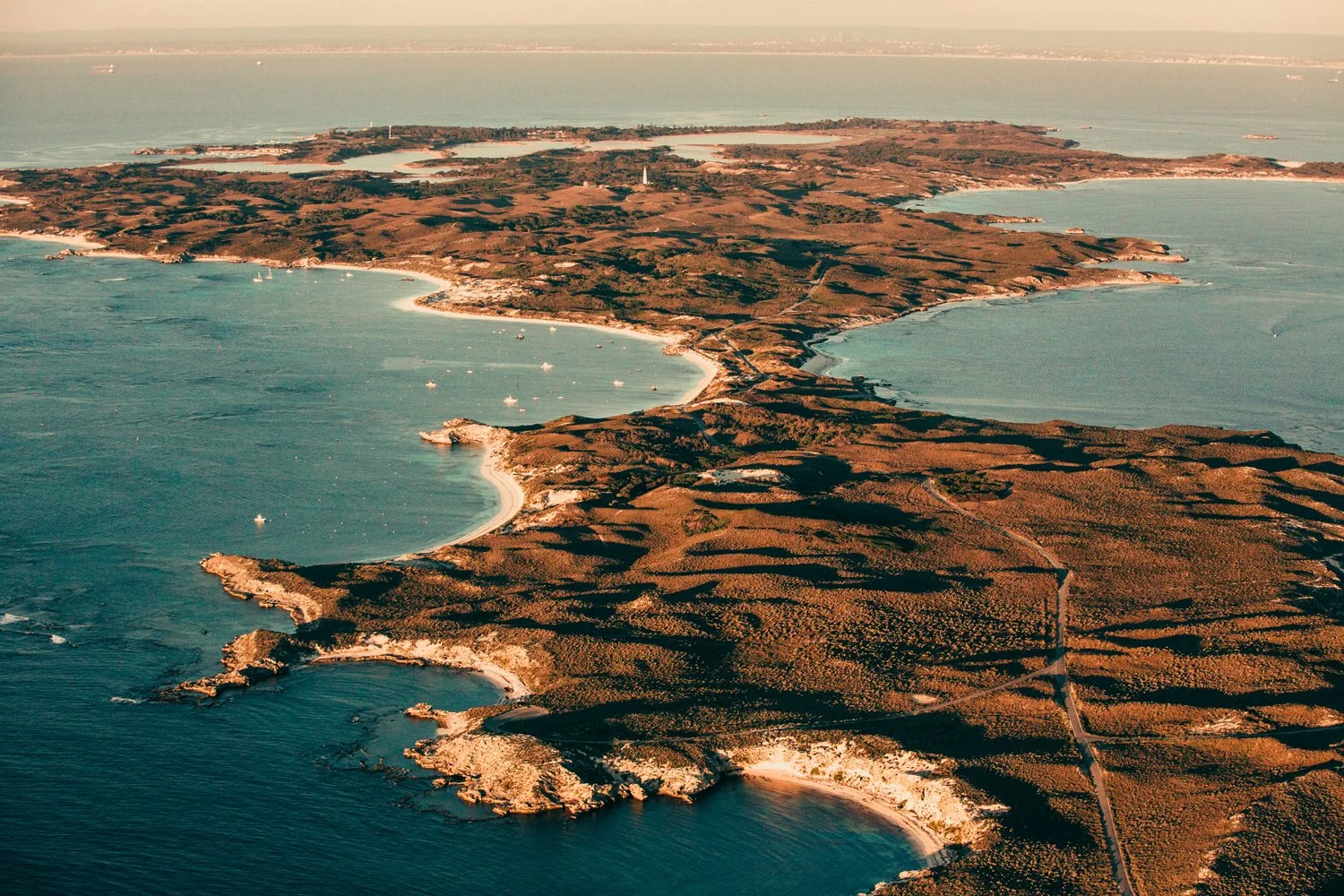 Aerial view of Rottnest island with rugged coastlines, surrounded by blue waters and boats.