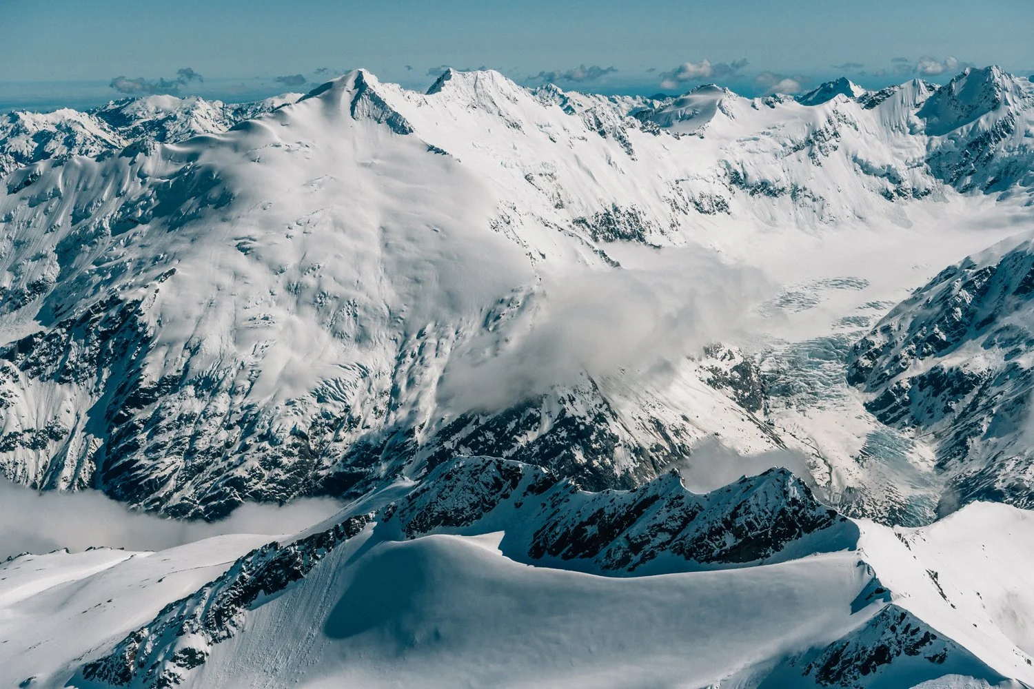 Snow-covered mountain range with steep peaks and glaciers, under a partly cloudy sky.