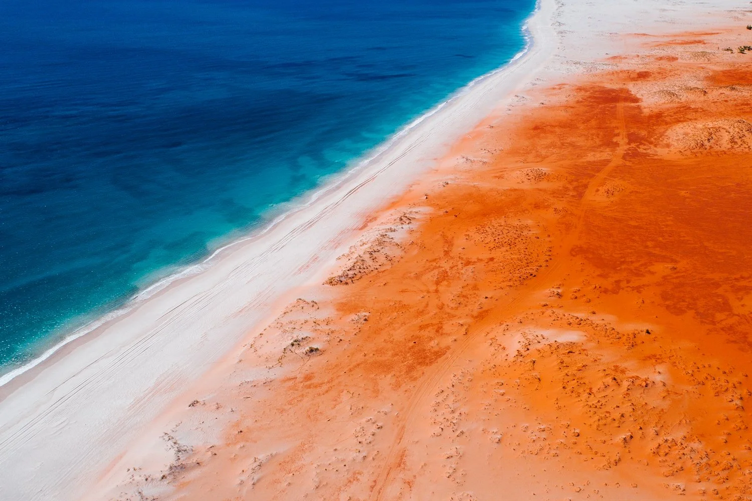 Aerial view of a beach with blue ocean water meeting orange and white sand dunes.