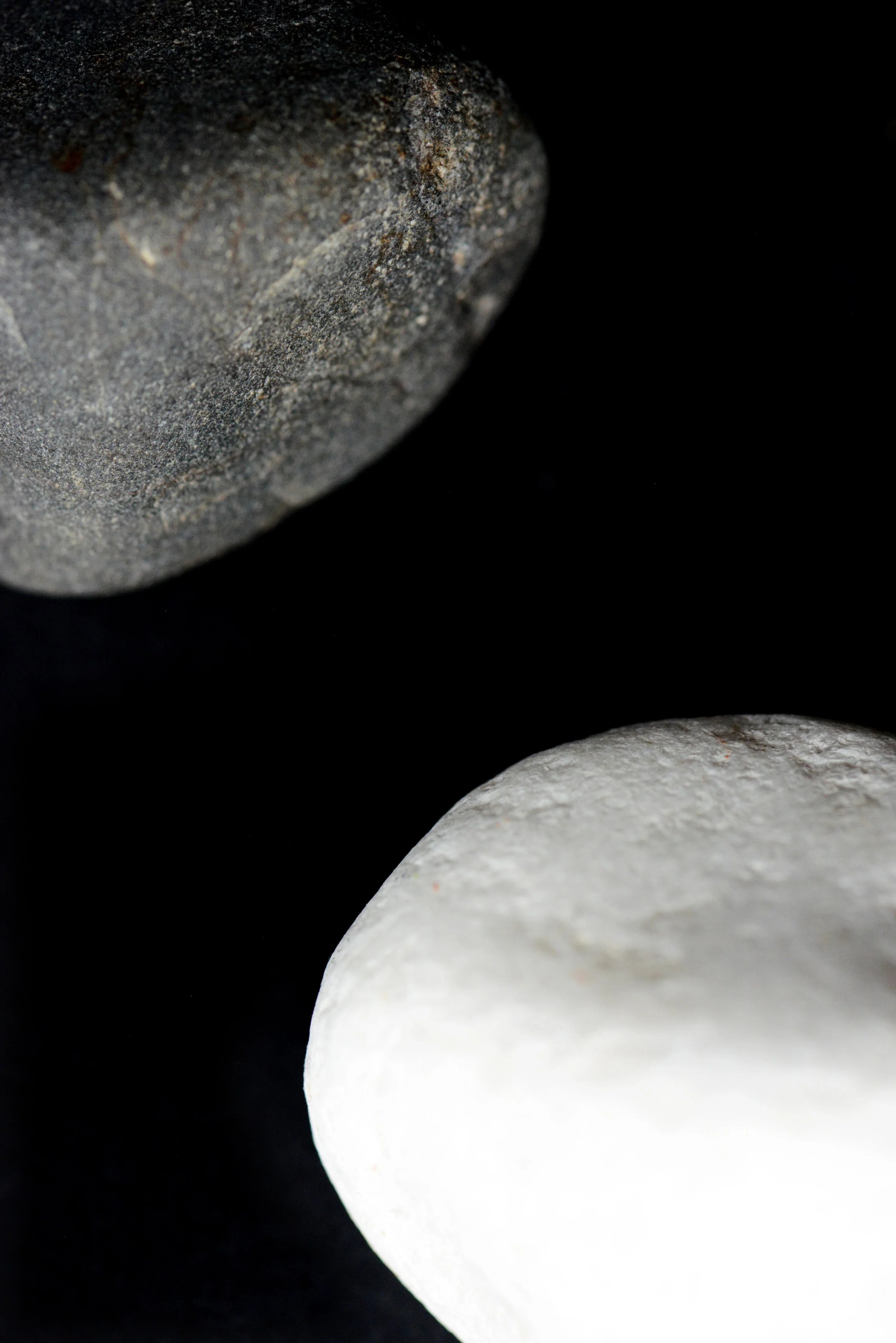Close-up of two stones, one black and one white, against a black background.