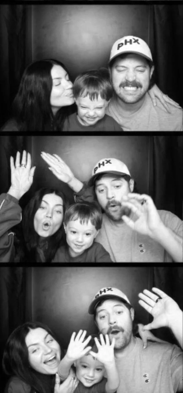 Black and white photo booth pictures of a family with a woman, a man wearing a hat, and a young boy. They are making funny faces and gestures in each frame.