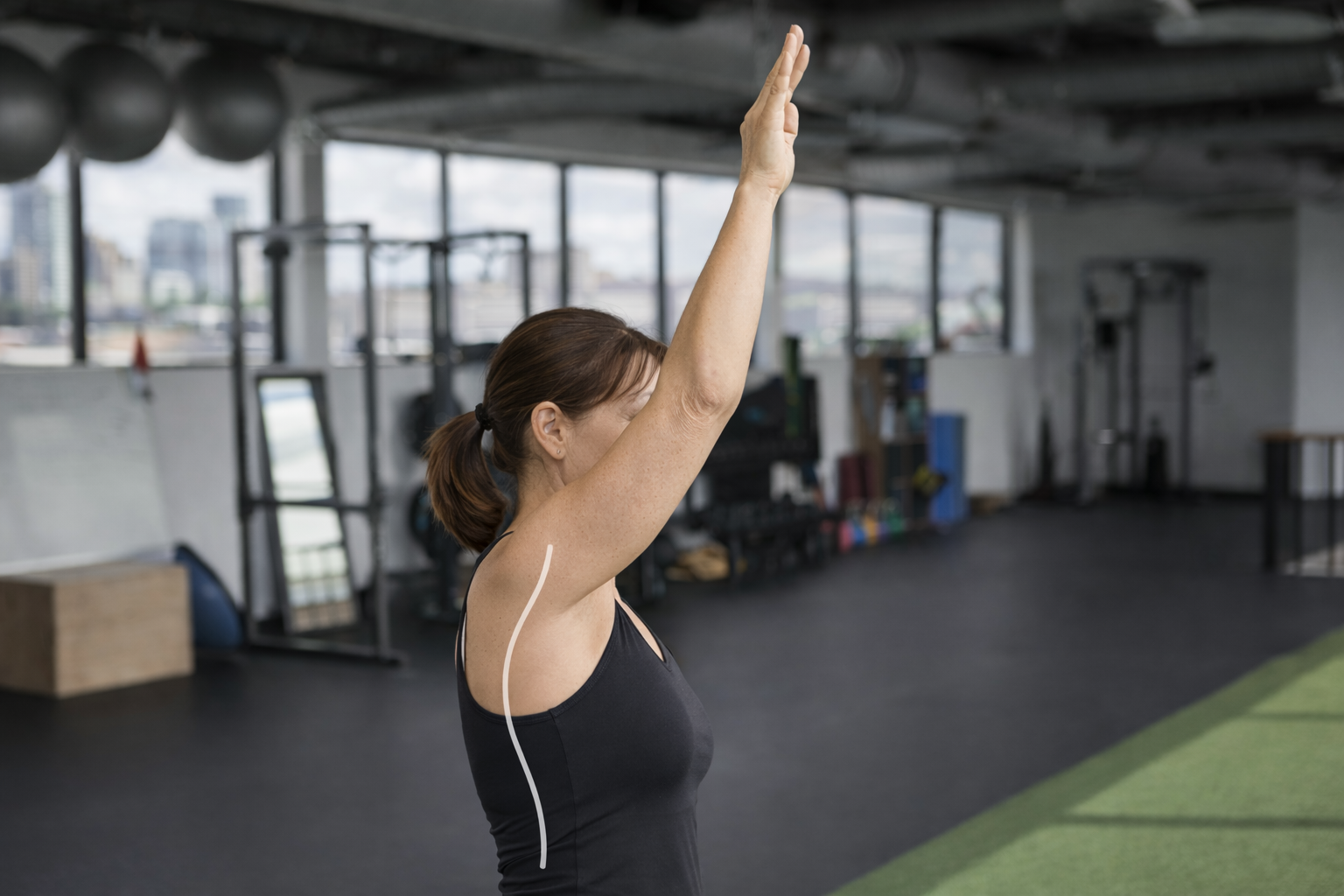 Woman performing an overhead reach with mild thoracic kyphosis demonstrating anterior shoulder load and postural contribution to shoulder pain.