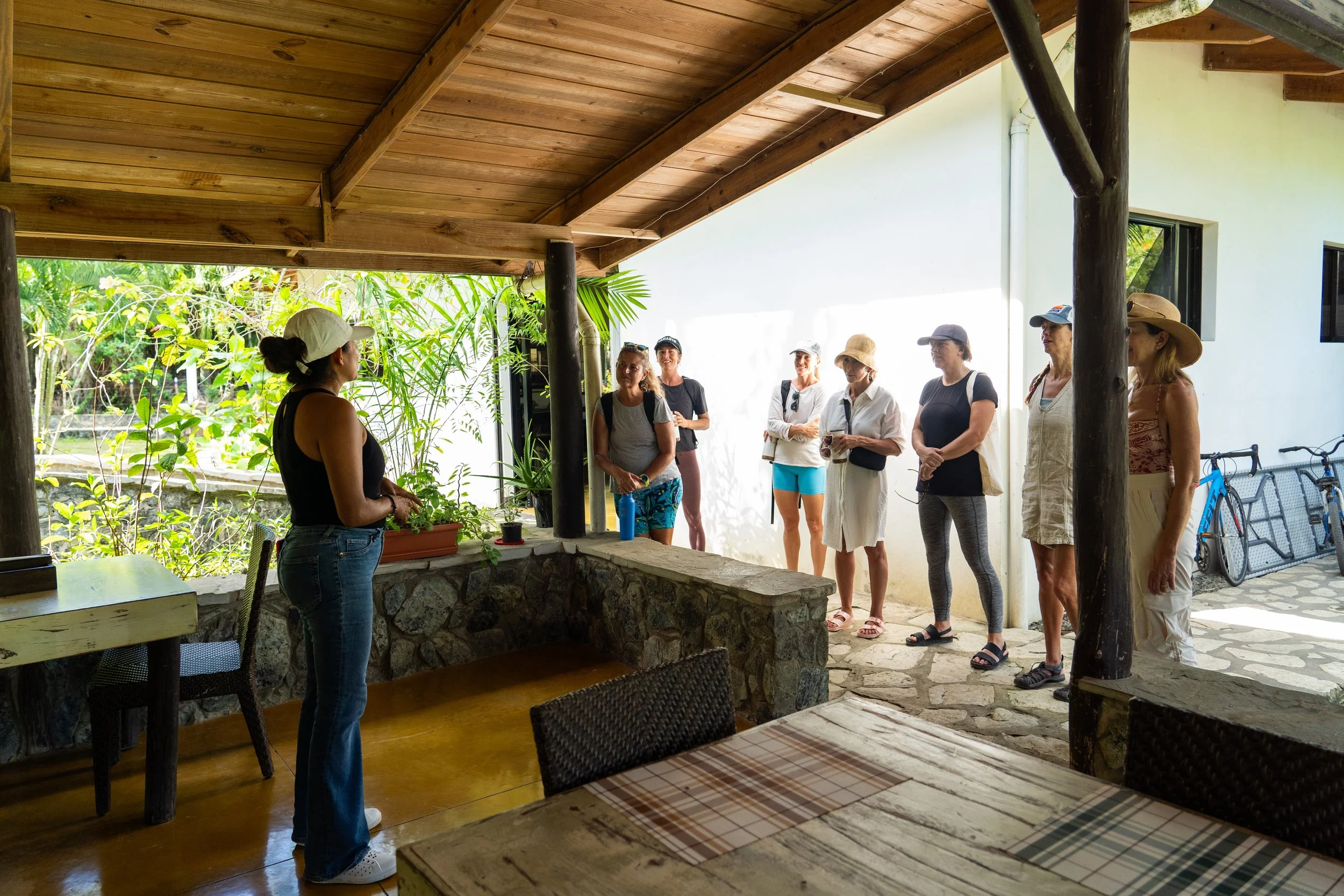 A woman giving a presentation to a group of women outdoors on a covered patio.