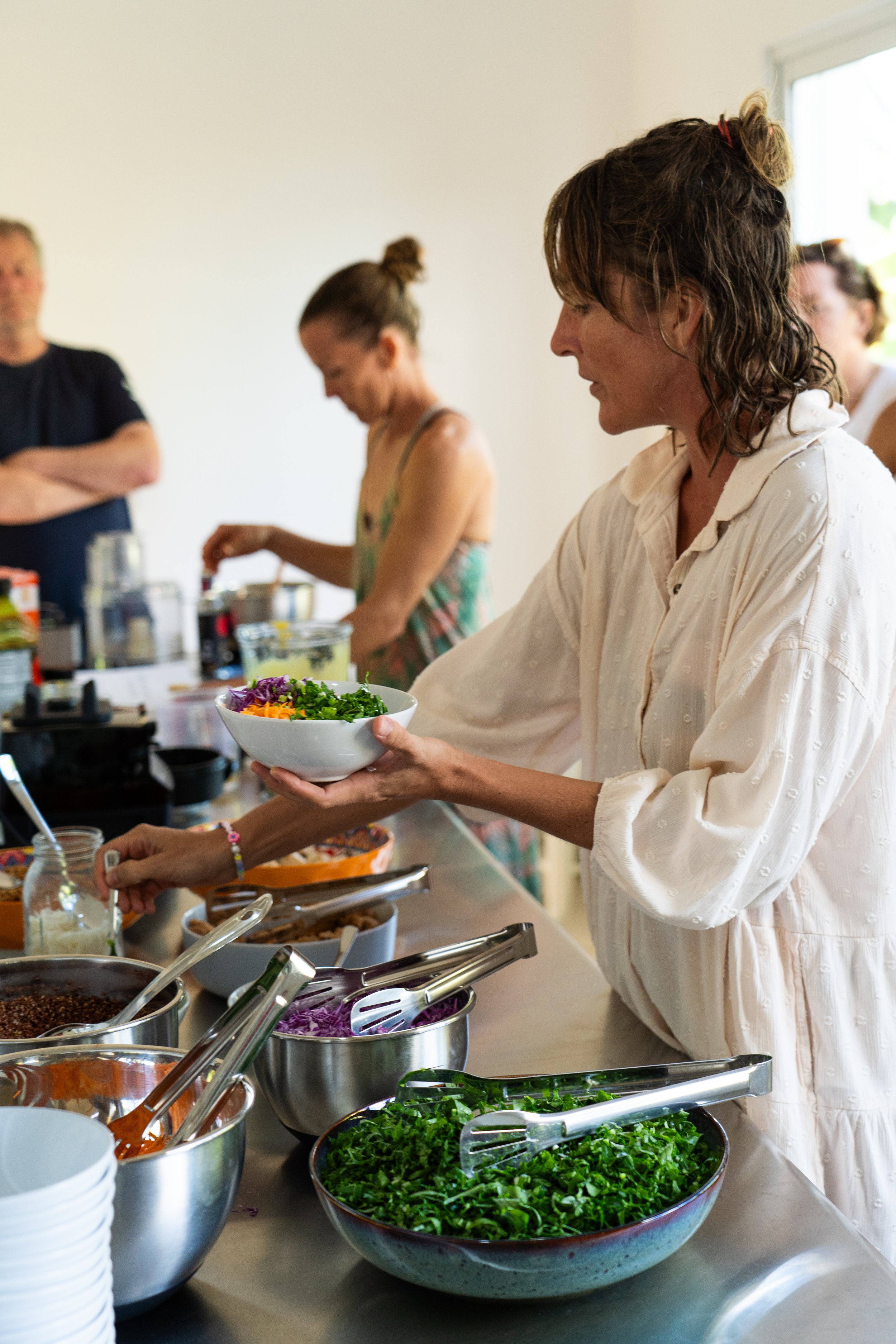 People serving themselves salad at a buffet with bowls of vegetables and toppings.