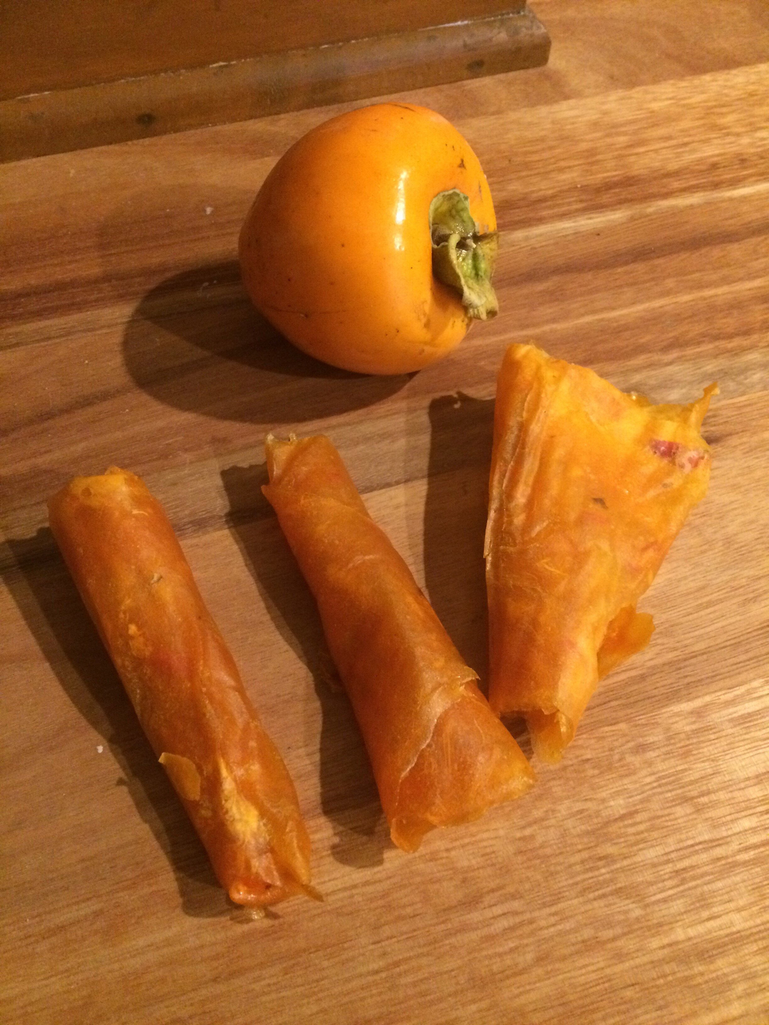 Fresh persimmon next to persimmon roll ups