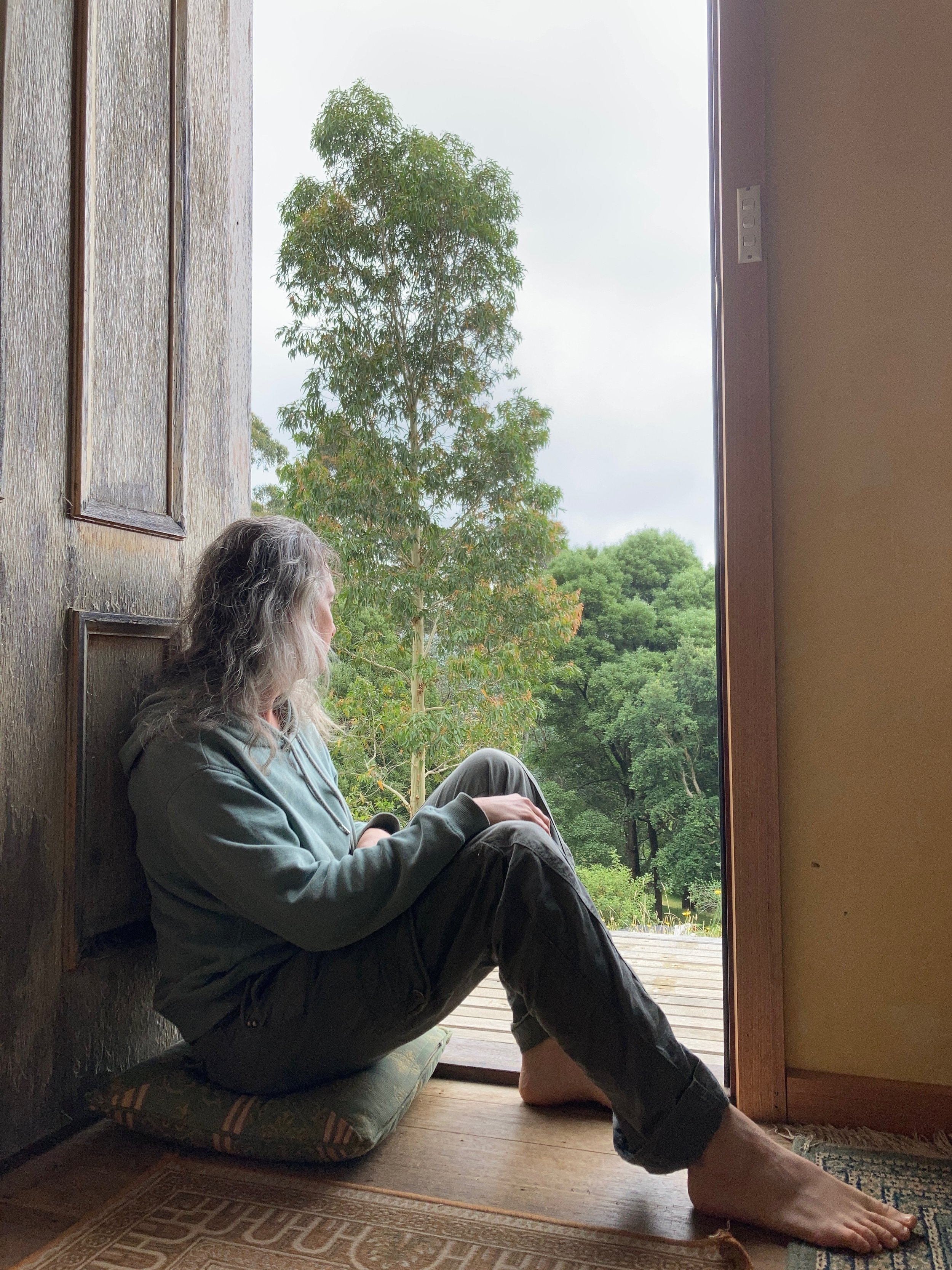 Woman sitting in doorway looking out at bush