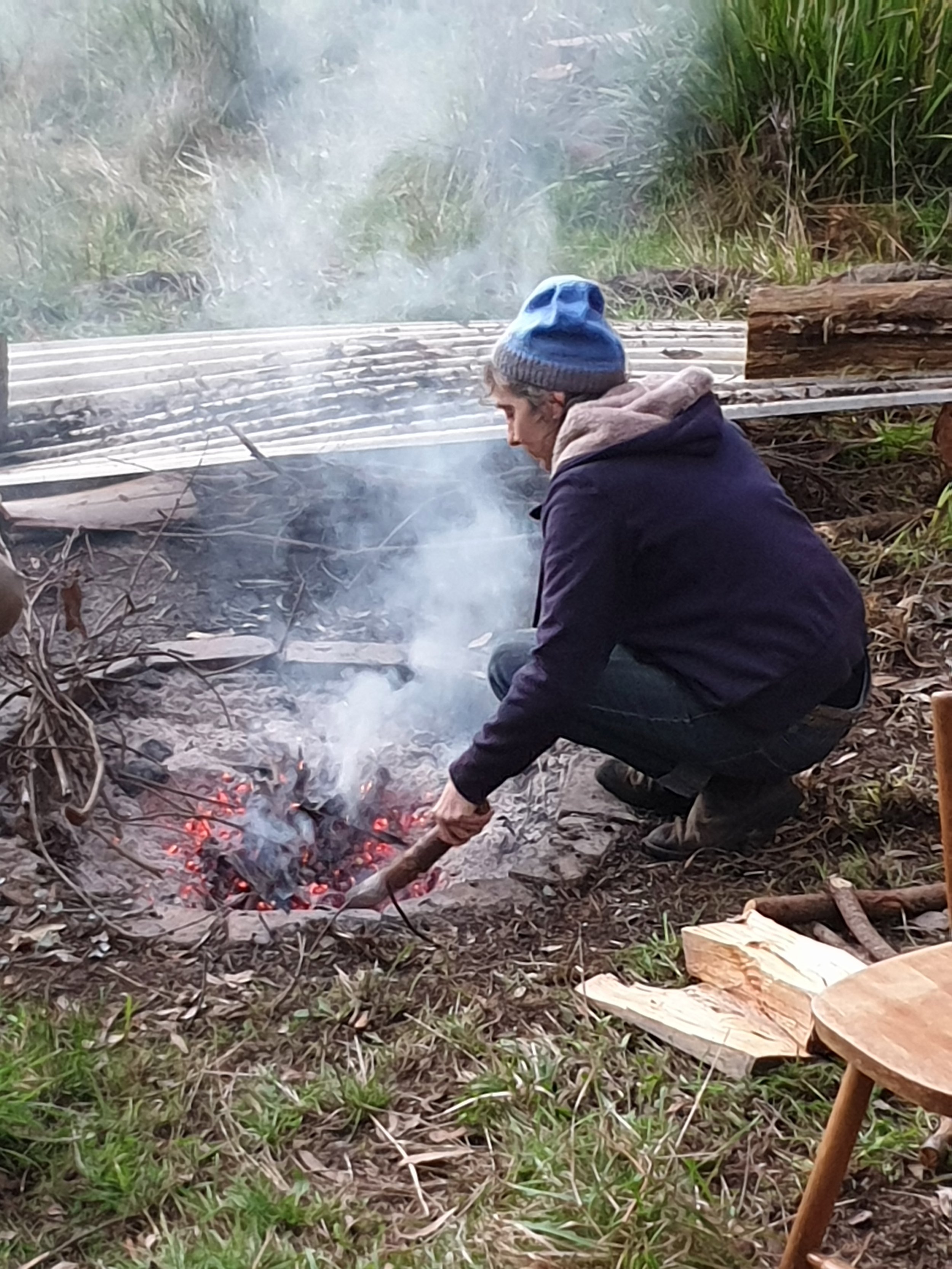 Woman in blue beanie poking campfire with stick