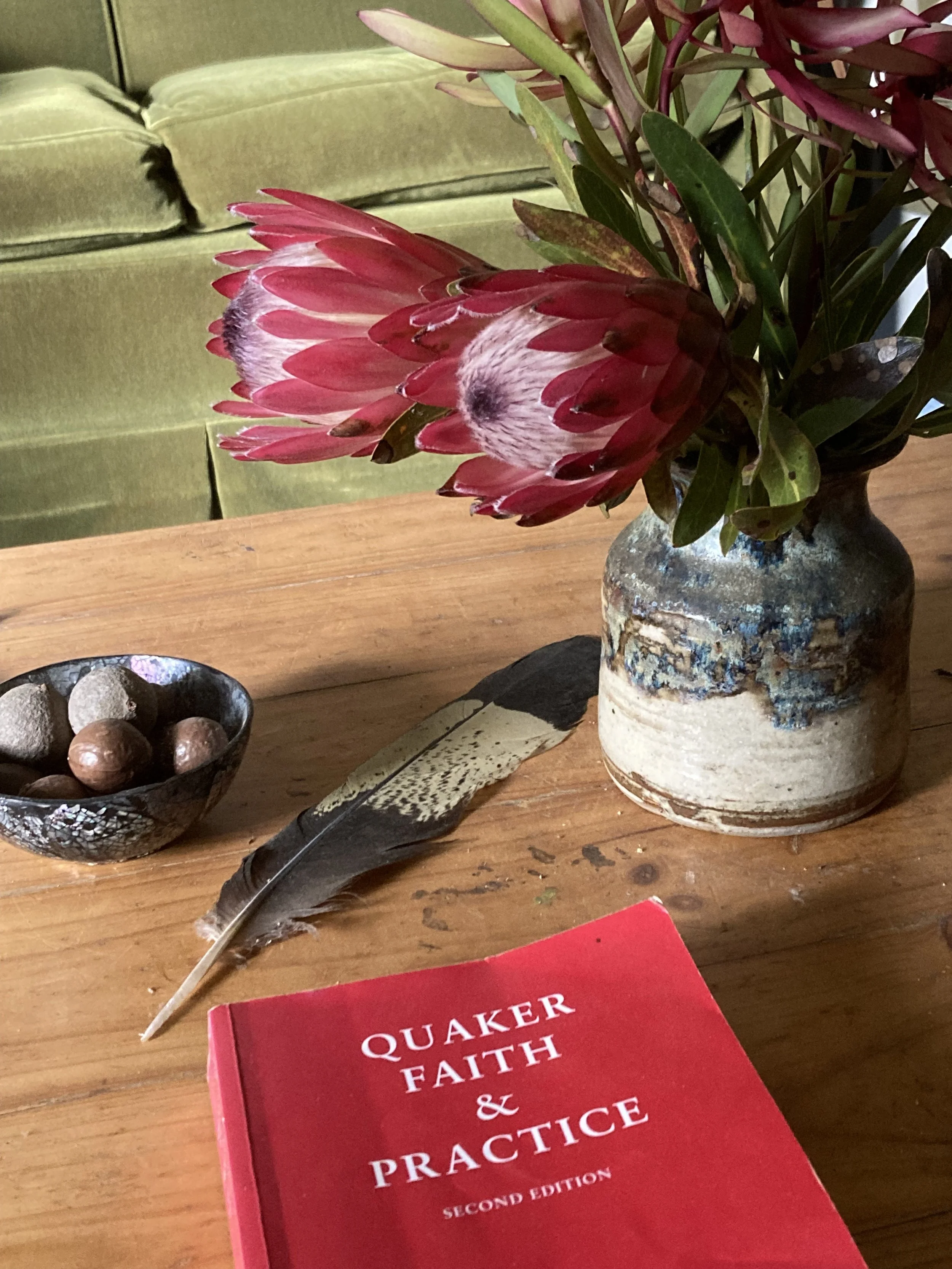 Red book titled 'Quaker Faith and Practice' next to vase of proteas and cockatoo feather