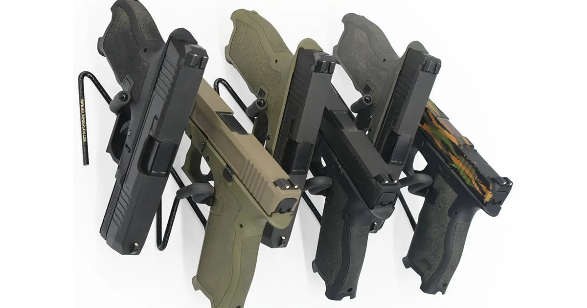 Six PSA Dagger Handguns of varying colors of black, green, and camo in a veritcal row placed on hangun stands against a white background.
