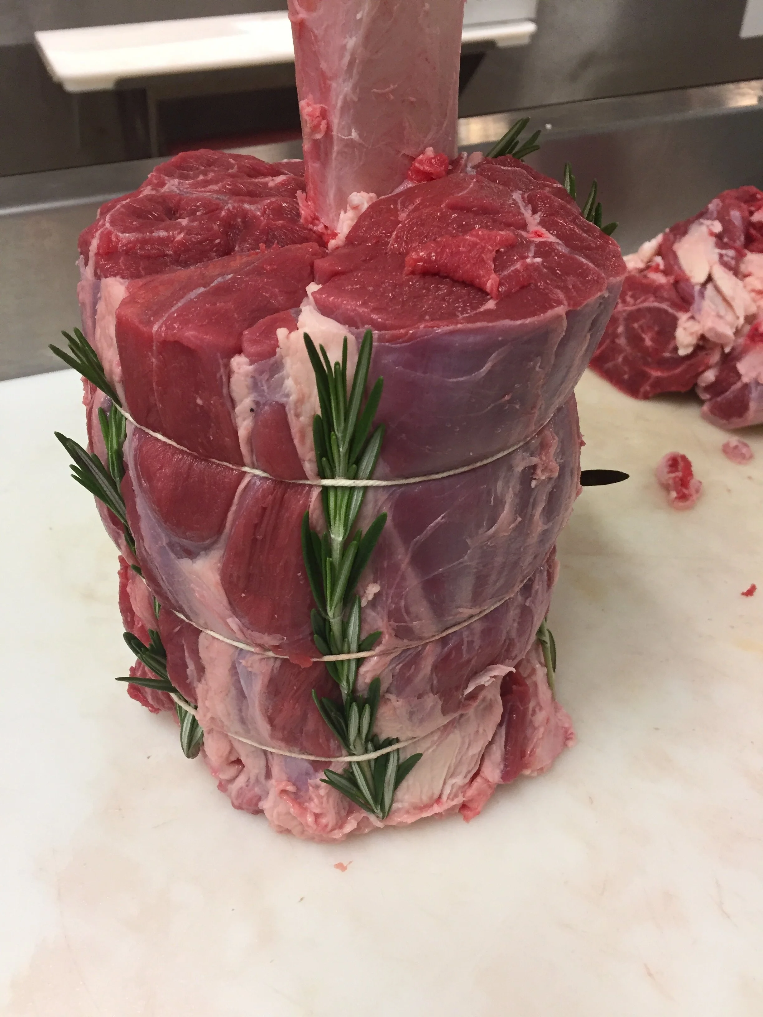 Stacked cuts of raw beef tied with string, garnished with sprigs of rosemary.