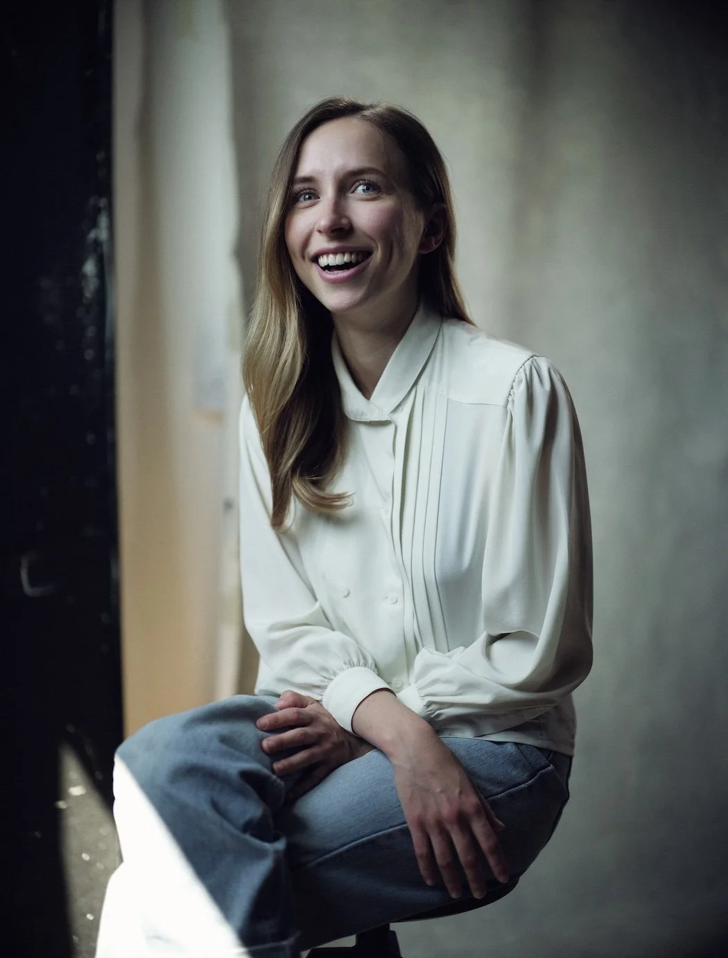 Woman smiling friendly, sitting down, white shirt, blue jeans