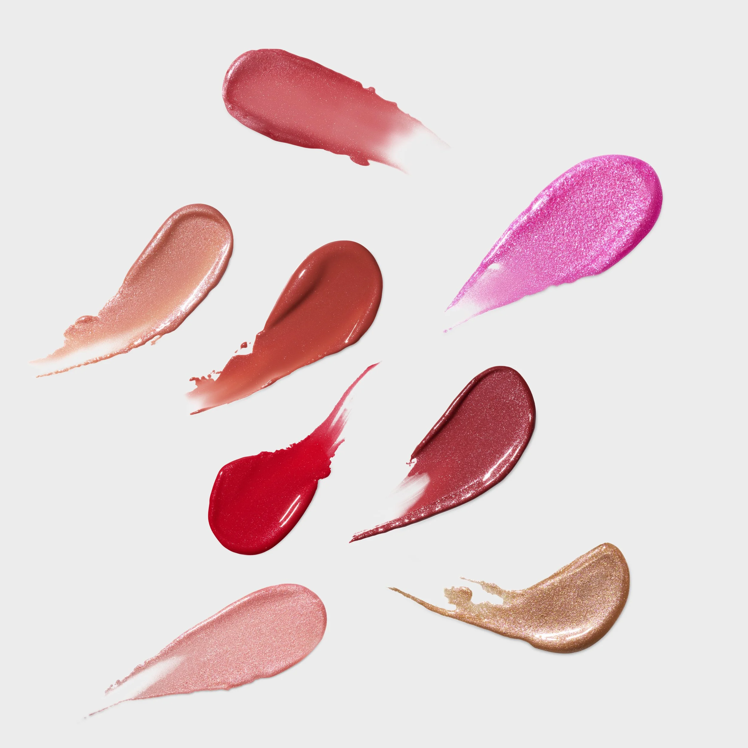 Swatches of various shades of lipstick in pink, red, nude, and gold on a light gray background. Product Photography. Creative Photography. eCommerce Photography.