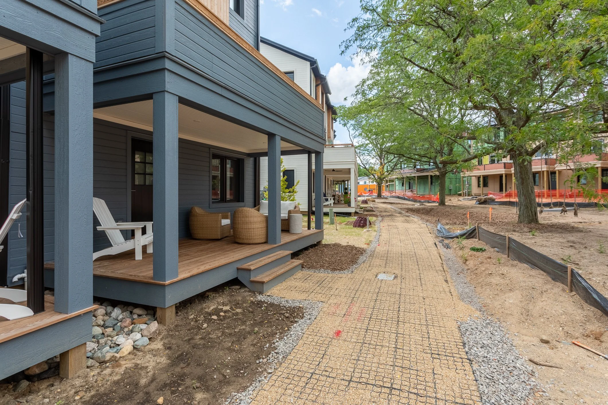Newly constructed residential houses with a sidewalk and trees, with some construction work ongoing in the area.