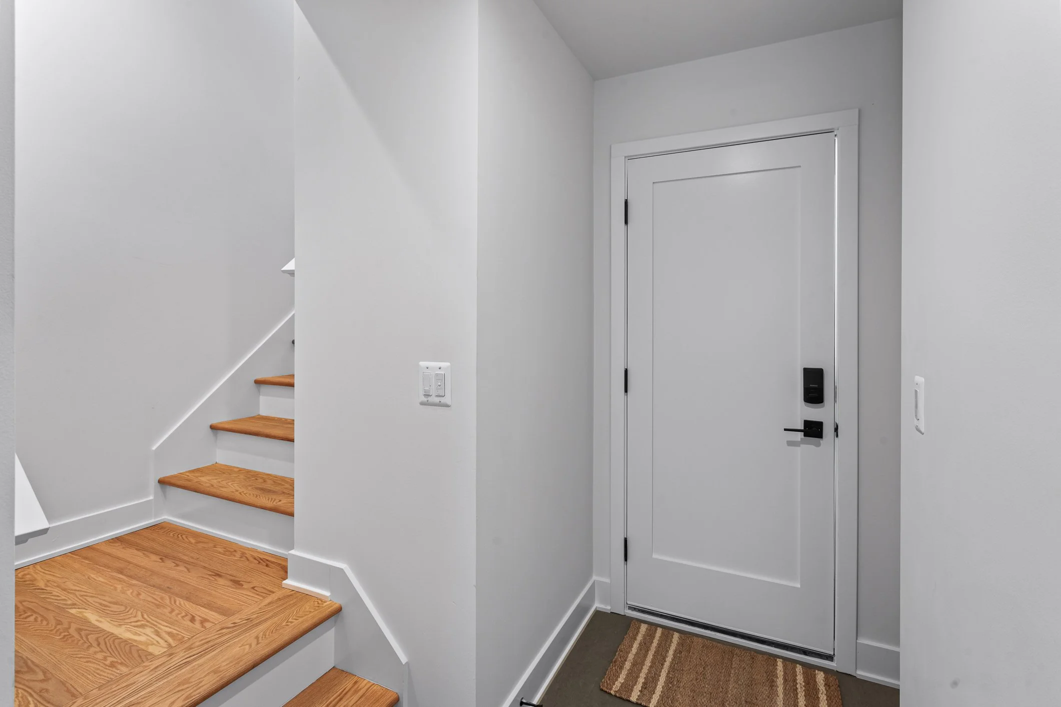 Interior of a house entryway with a white door, brown striped rug, and wooden stairs with white risers.