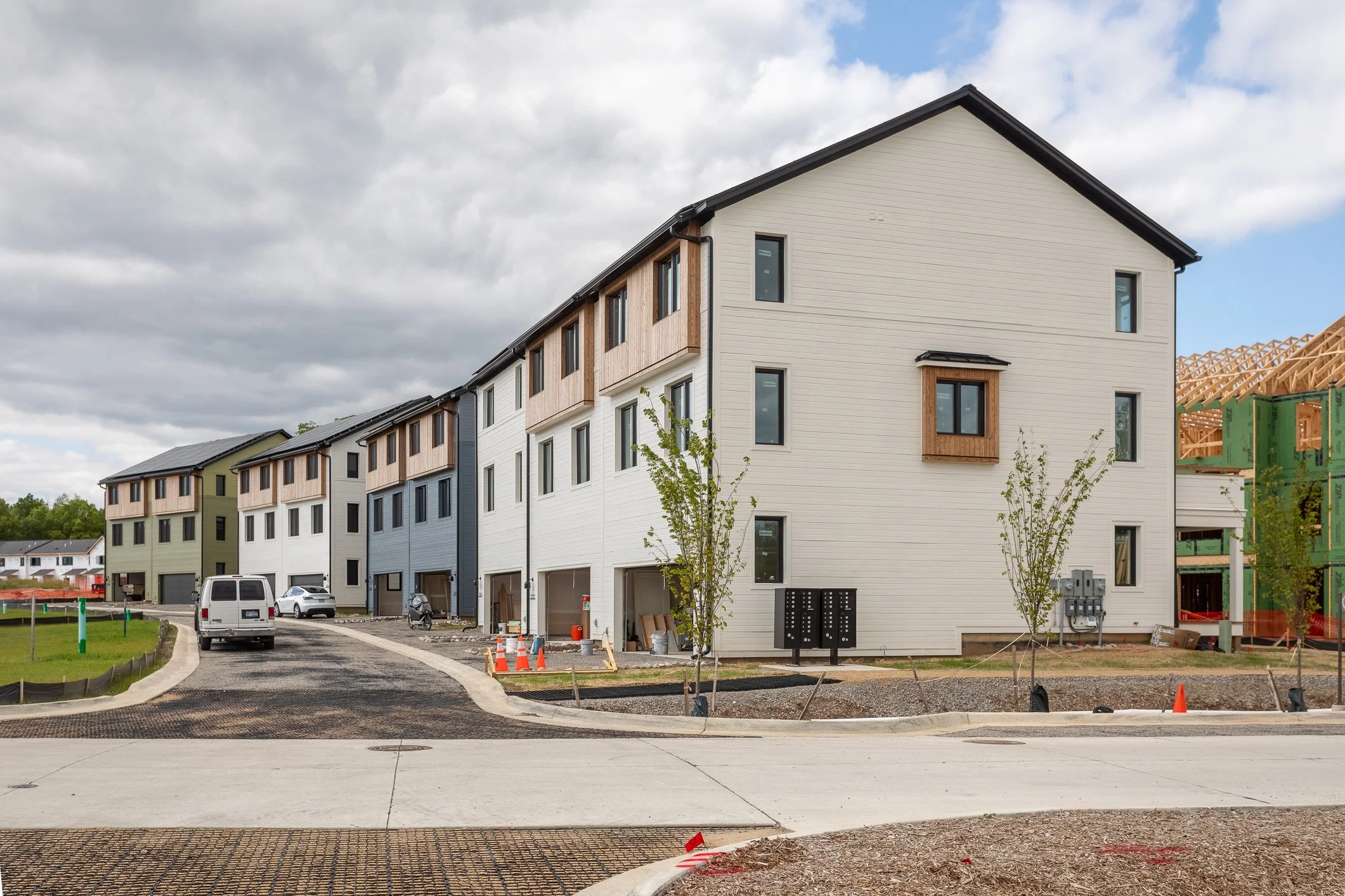 Newly constructed multi-story residential building with white siding, wooden accents, and garage spaces, with construction equipment and new landscaping.