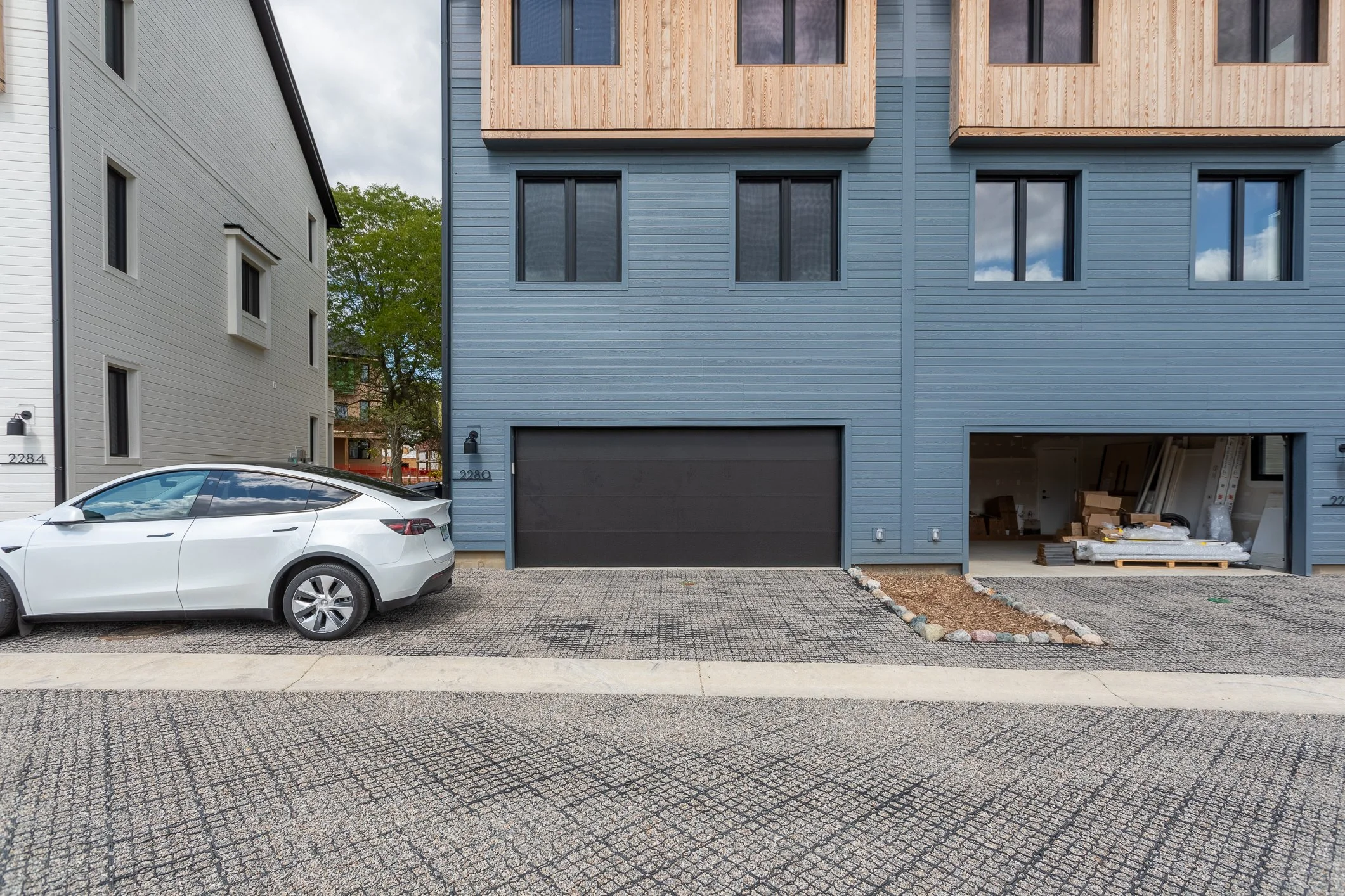 Modern townhouse with a blue exterior and a two-car garage, with construction materials visible inside and a white electric car parked in front.
