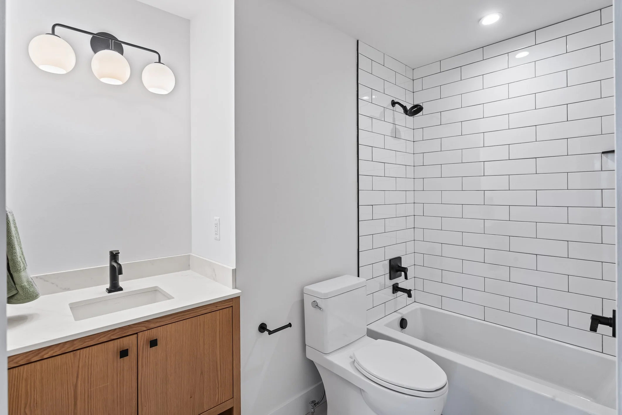 Modern bathroom with white subway tile shower, black fixtures, wooden vanity with white countertop, and a mirror with three white globe light fixtures.