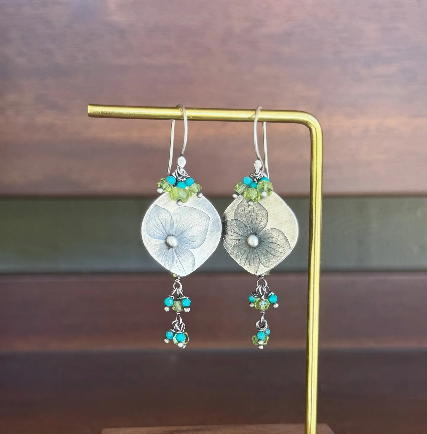 Handcrafted fine silver earrings featuring delicately imprinted hydrangea blooms, paired with wire-wrapped turquoise and peridot gemstones for a soft pop of color. 
#handmadejewelry #metalsmith #handmadeearrings #turquoise #hydrangeajewelry #summerje