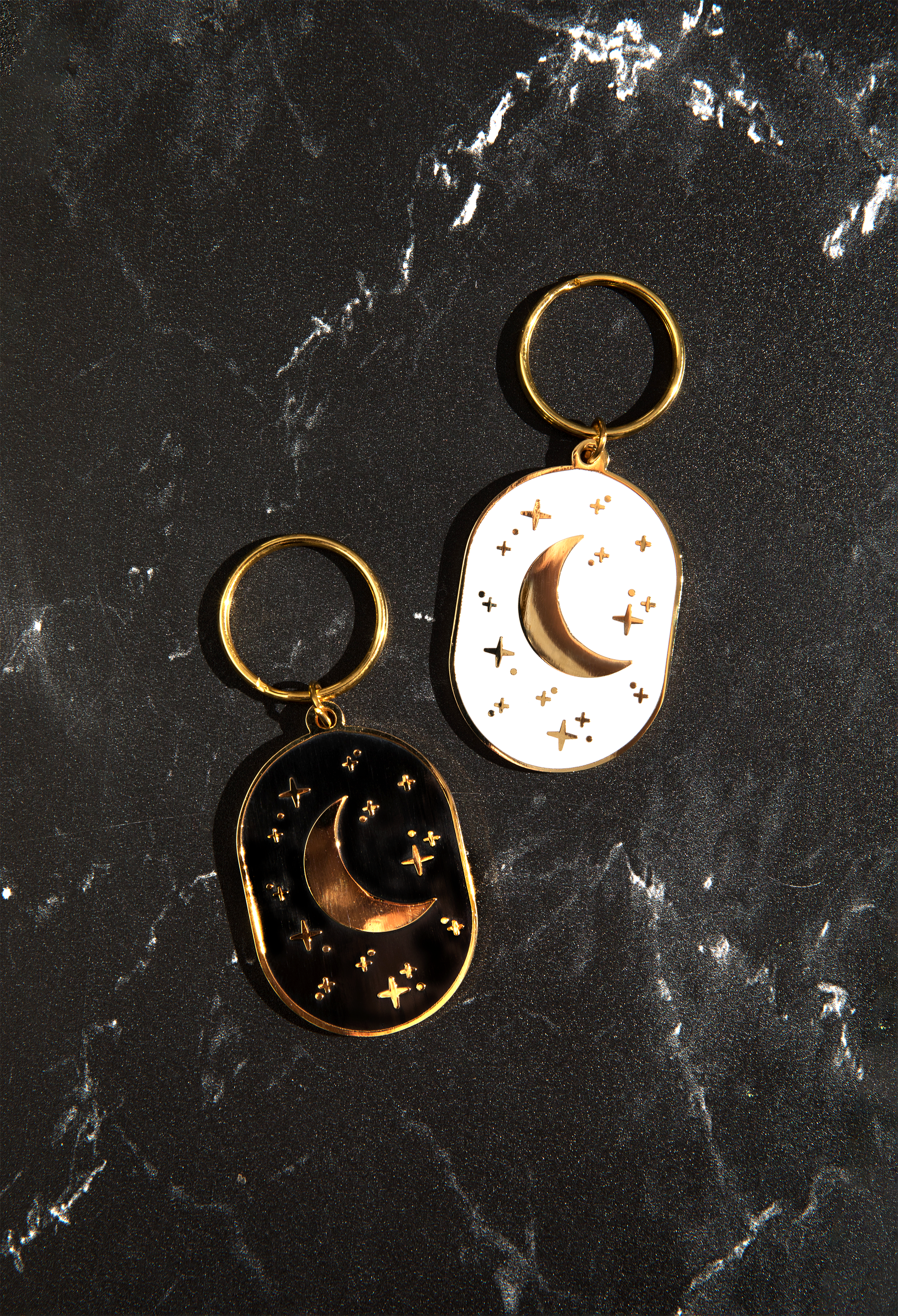 An oval, double-sided white keychain featuring a night sky with a crescent moon and twinkling stars.