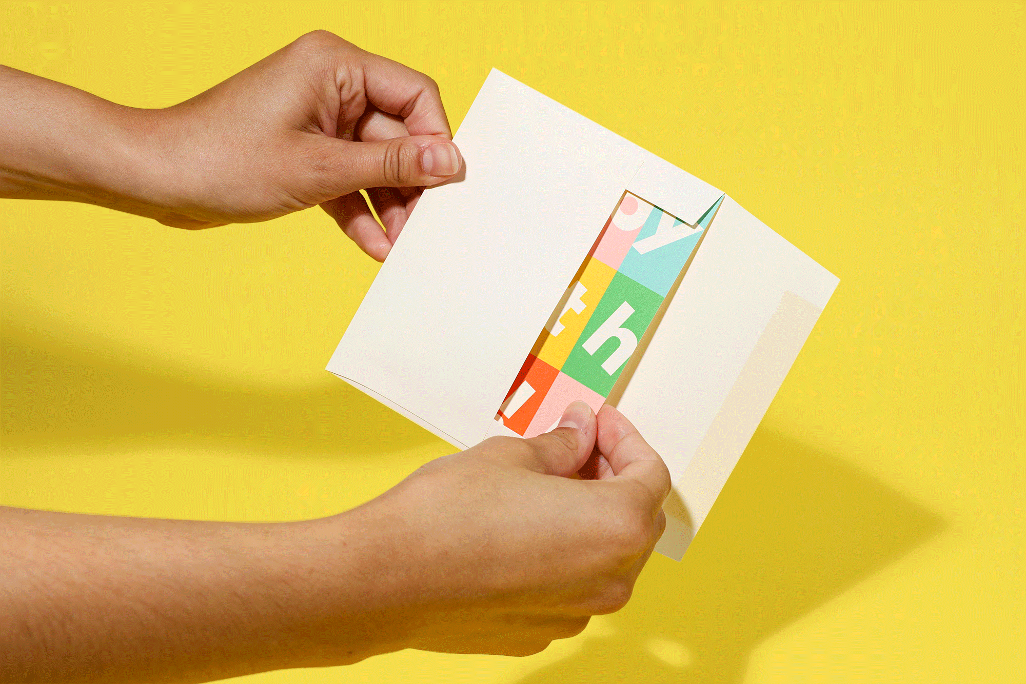 Person holding a greeting card with colorful, abstract geometric design on the inside, against a yellow background.