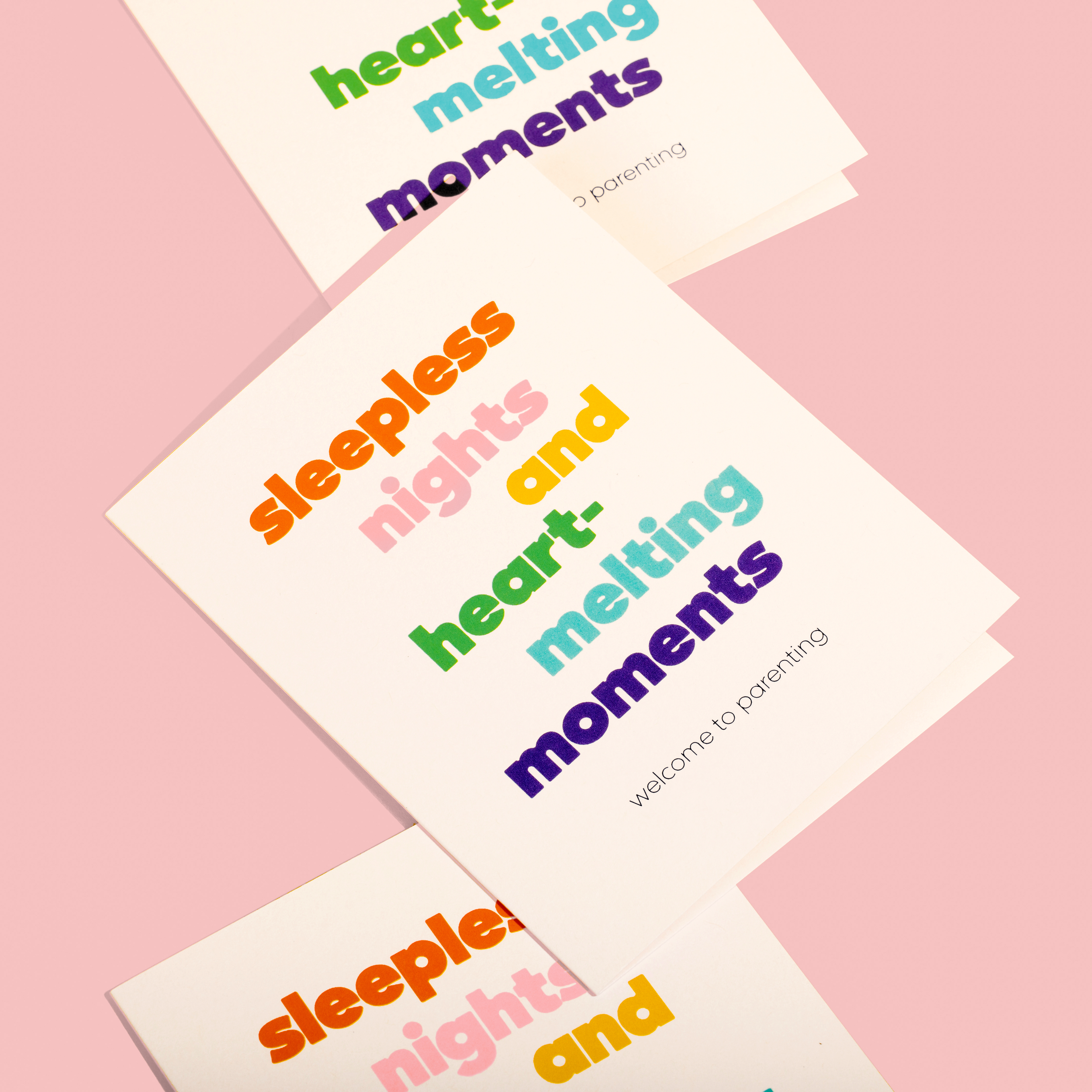 Stacked greeting cards with colorful text reading 'sleepless nights and heart-melting moments' on a pink background, welcoming new parents.