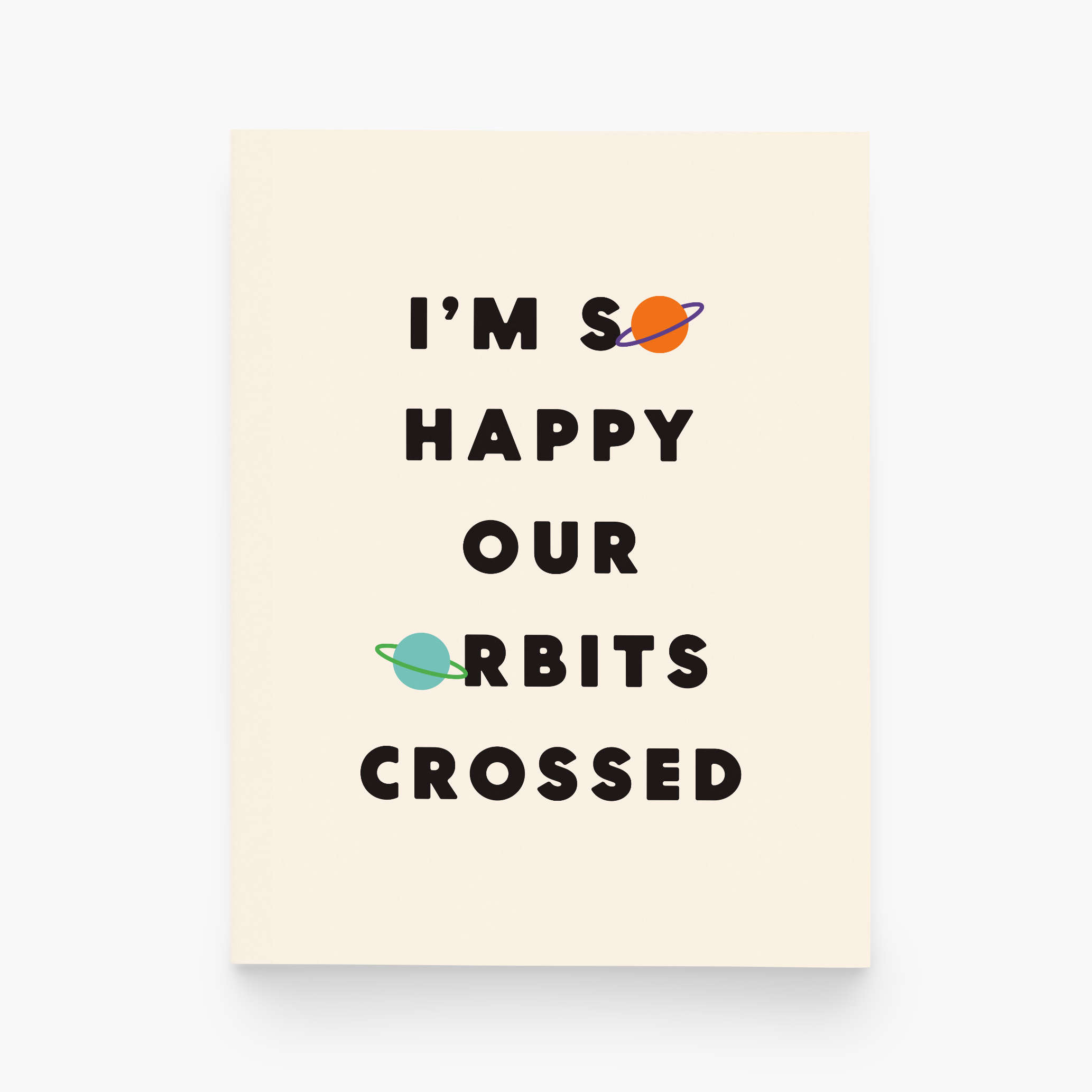A cream greeting card with the black text "I'M SO HAPPY OUR ORBITS CROSSED" and the 'o' in 'so' and 'orbits' are planets.