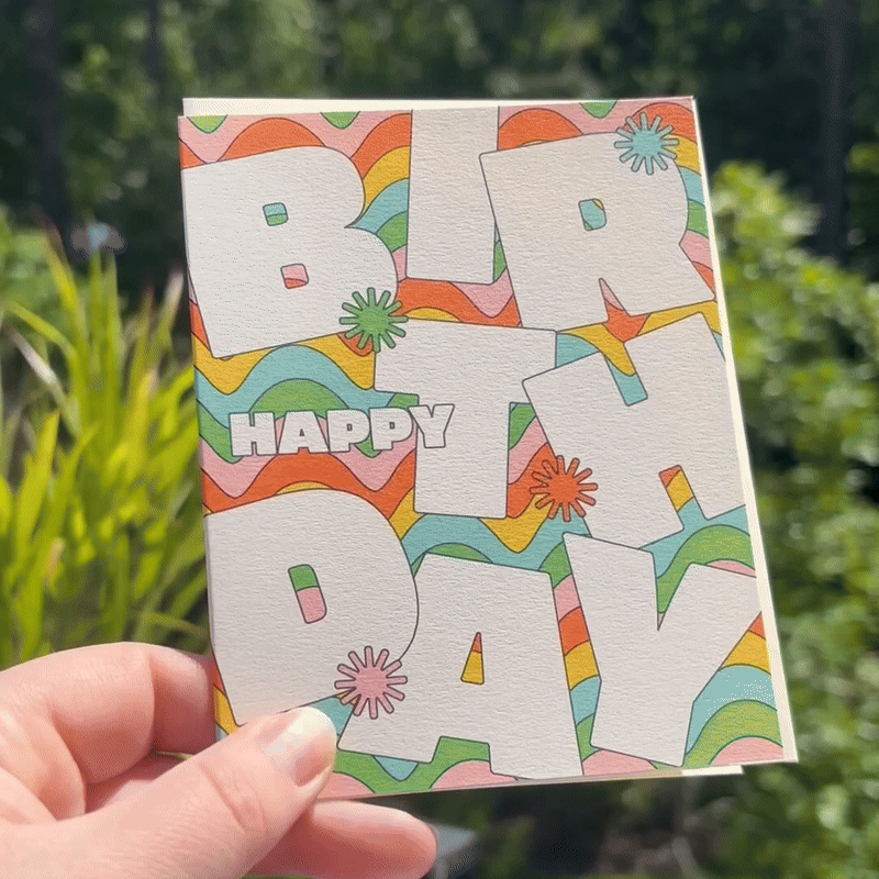 A GIF of the Wavy Typography card is being held in front of greenery.