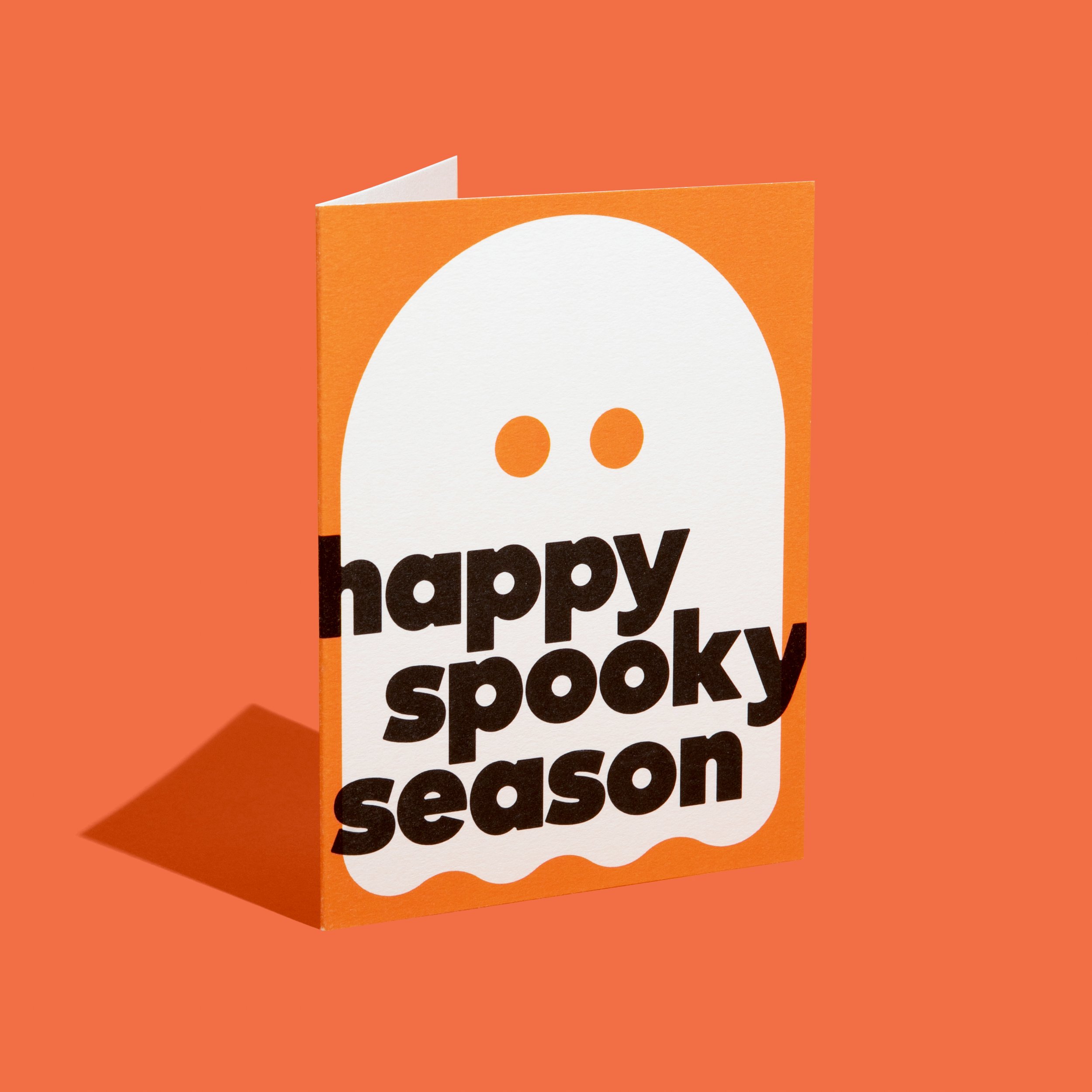 A greeting card with an orange background featuring a simple ghost illustration and the text 'happy spooky season' in bold black letters, set against a matching orange backdrop.