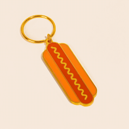 Hot dog-shaped keychain with yellow mustard design on orange background