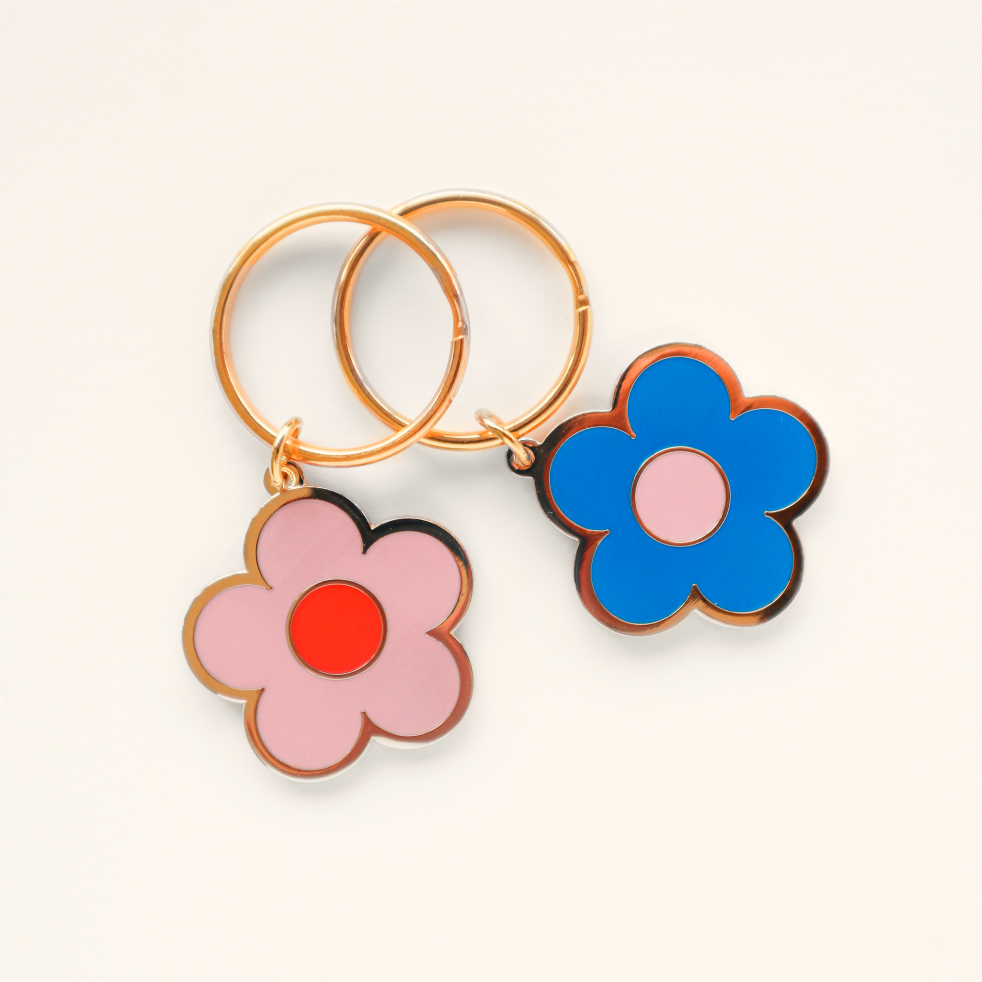Two flower-shaped keychains with gold rings, one with a pink flower and red center, the other with a blue flower and pink center.
