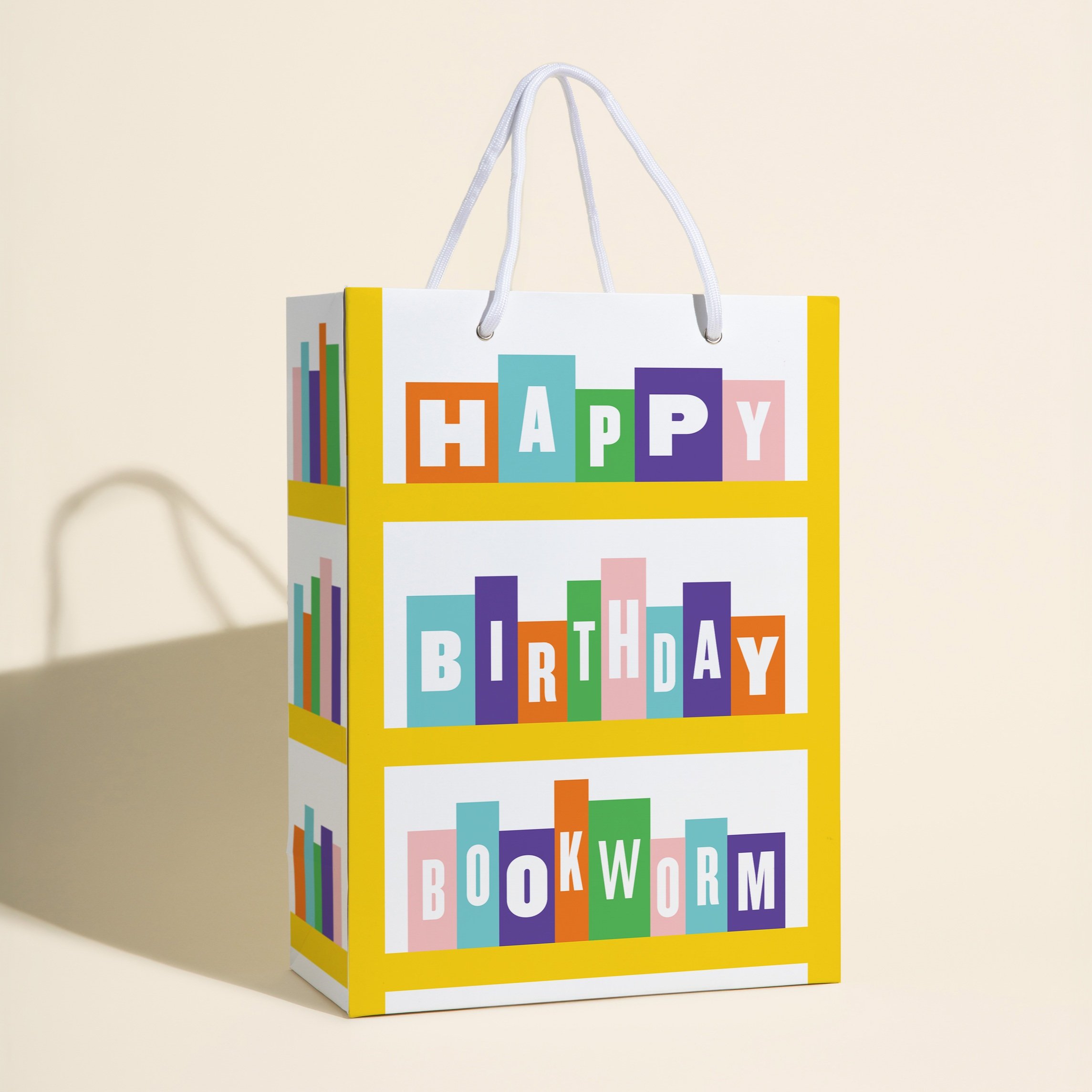 Gift bag with a "Happy Birthday Bookworm" message, designed with a bookshelf-inspired graphic featuring multicolored books stacked vertically on a bright yellow frame.
