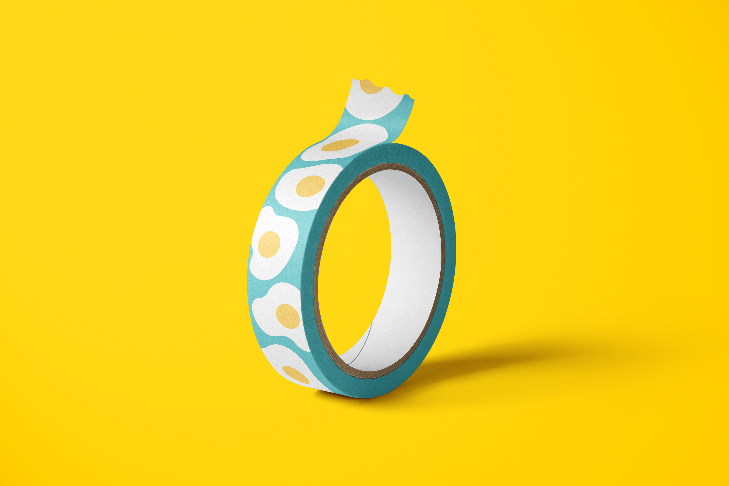 Roll of decorative washi tape with a teal background and fried egg pattern, set against a bright yellow backdrop.