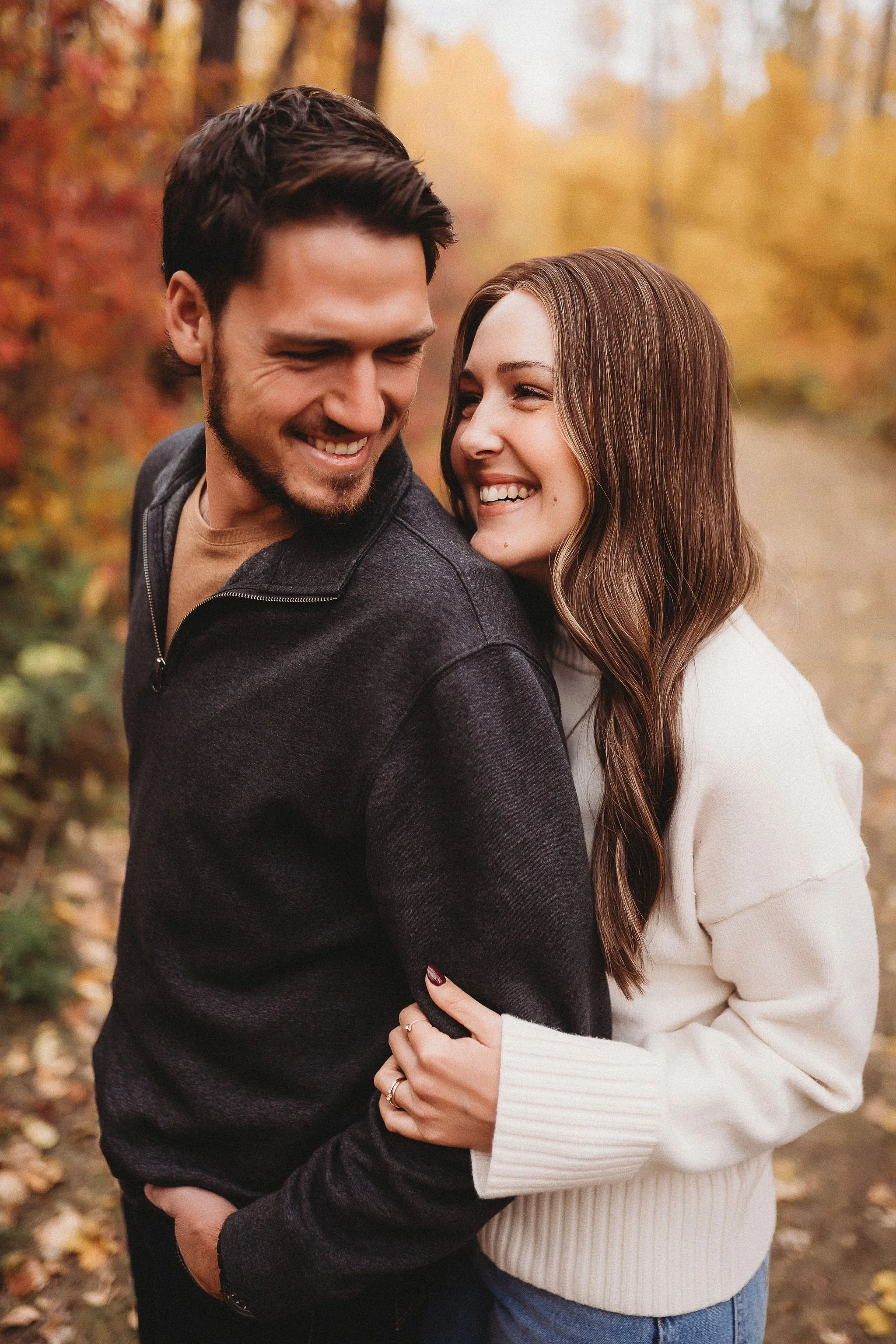 A happy couple hugging outdoors during autumn, with fall foliage in the background.