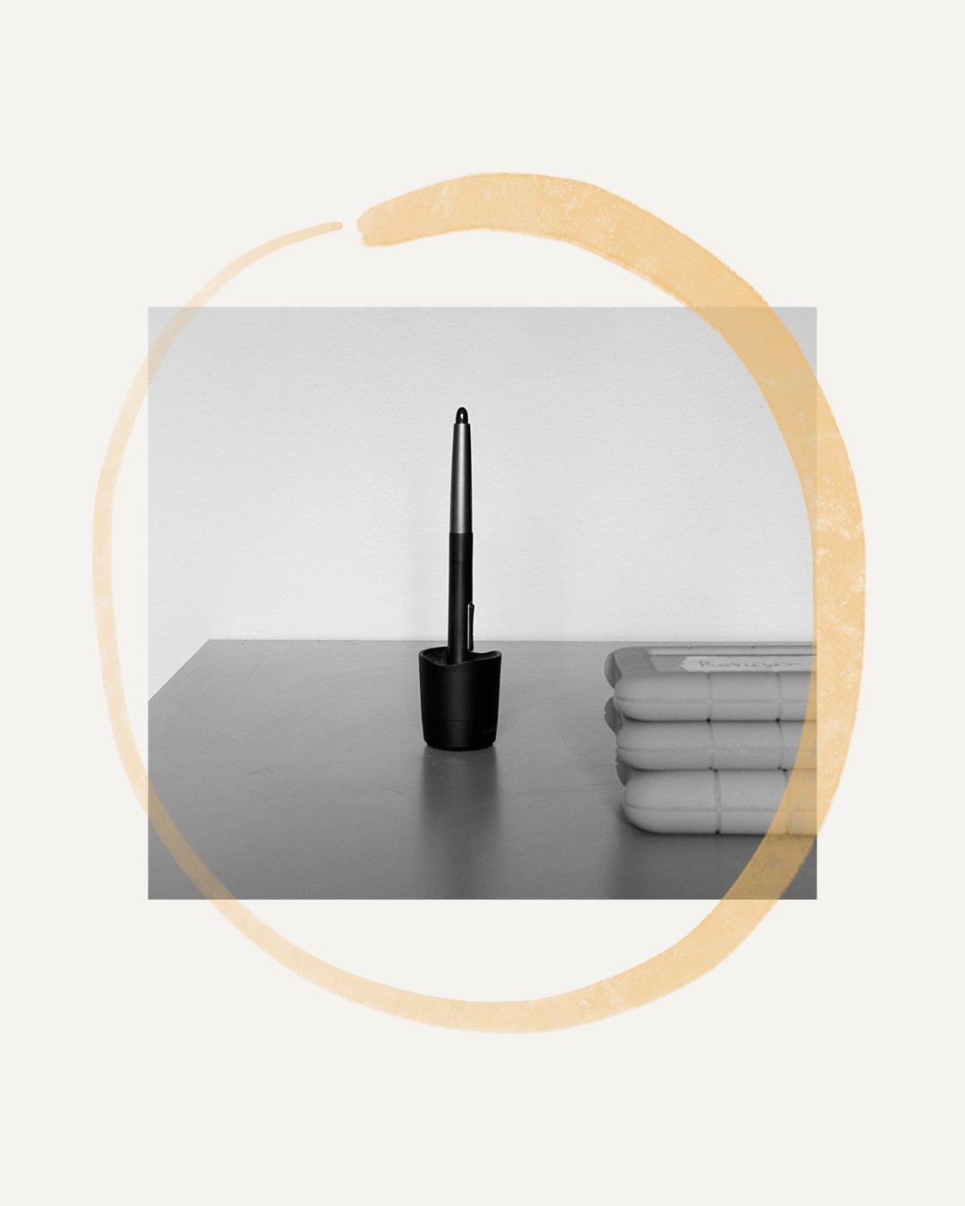 A black pen in a pen holder and a stack of white notebooks on a desk against a plain white wall.