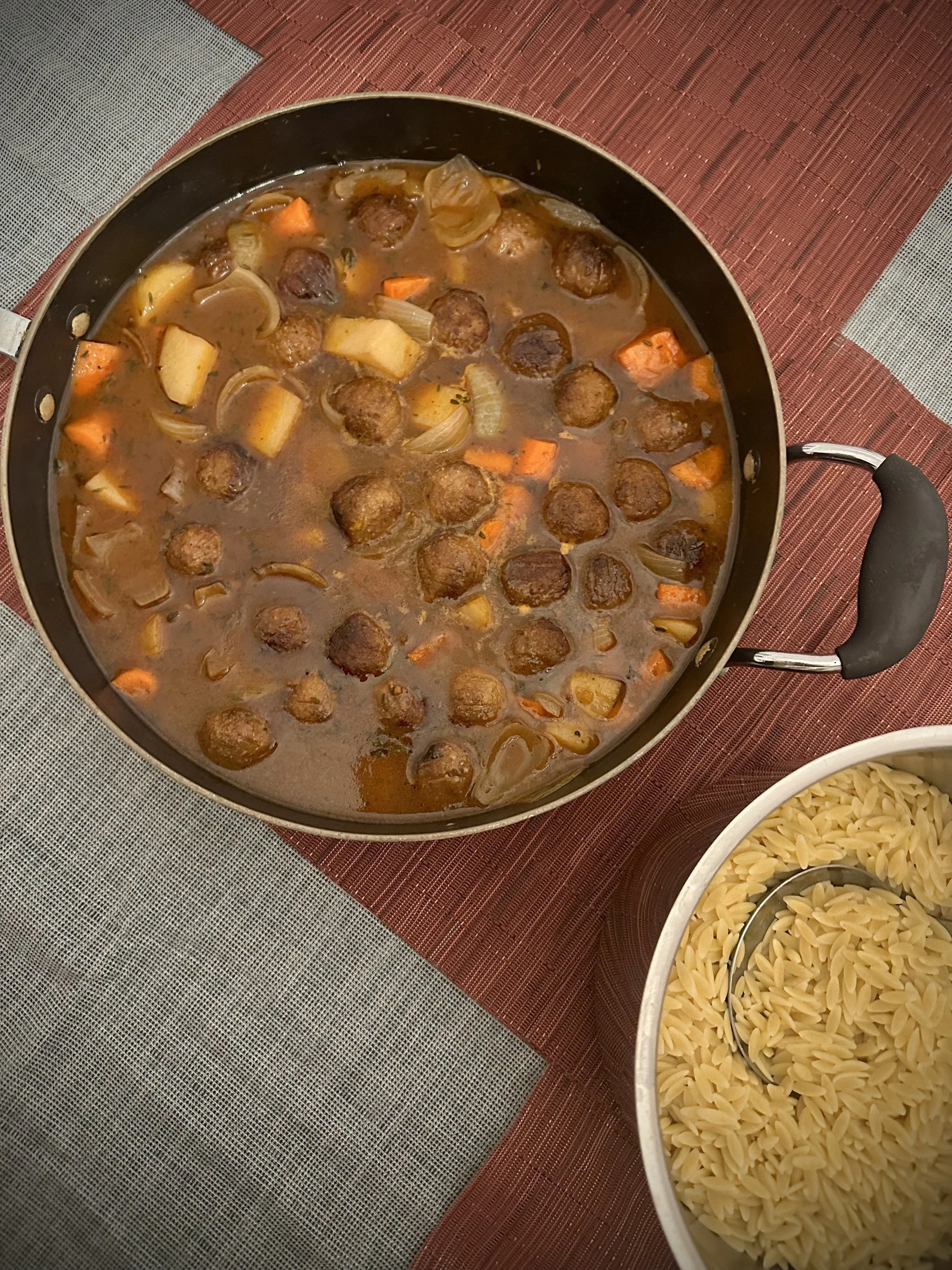 A pot of cooked meatball and vegetable stew alongside a bowl of uncooked rotini pasta.