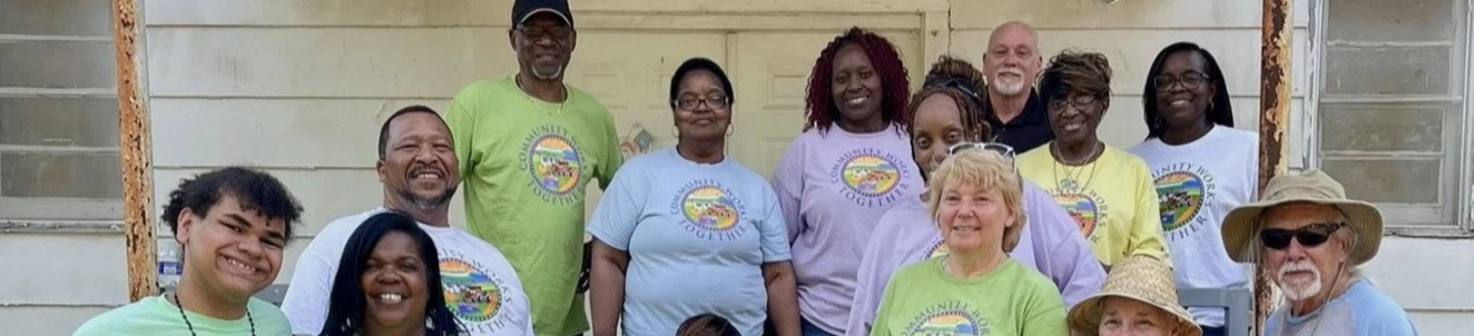 Group of diverse people posing outside a building with white walls, wearing colorful t-shirts and some wearing hats, smiling for a photo.