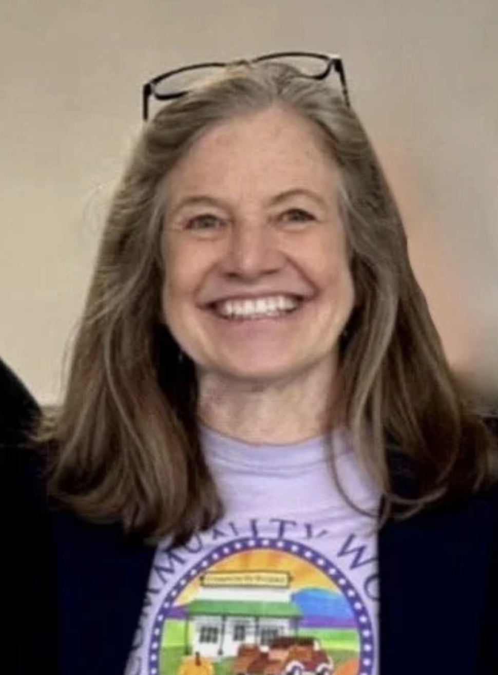 A woman with glasses on her head, smiling, wearing a T-shirt with a colorful design, and a dark blazer.
