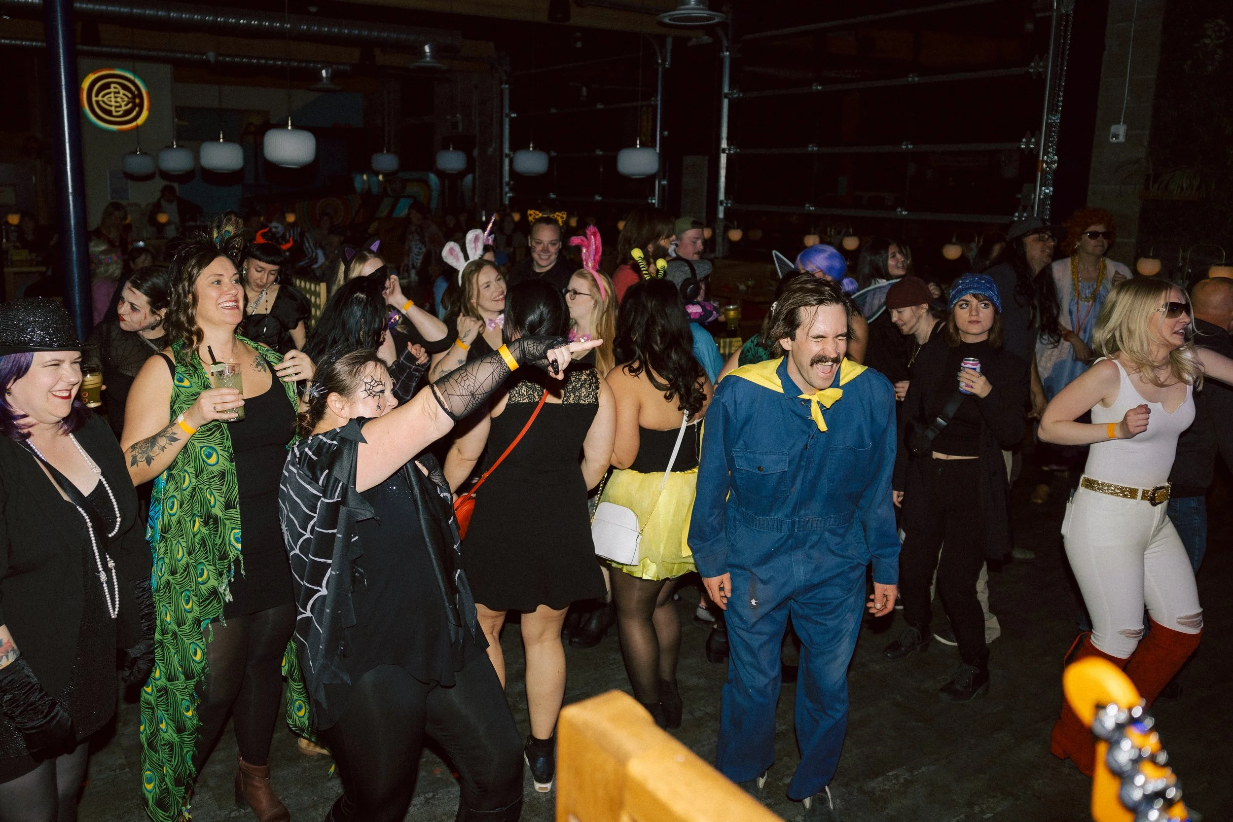 People dressed in Halloween costumes enjoying a party and dancing in a dimly lit indoor venue.