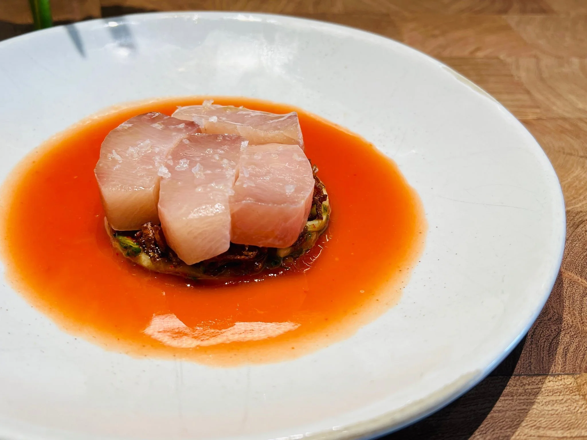 Sashimi slices on a bed of vegetables served with a tomato-based sauce in a white bowl.