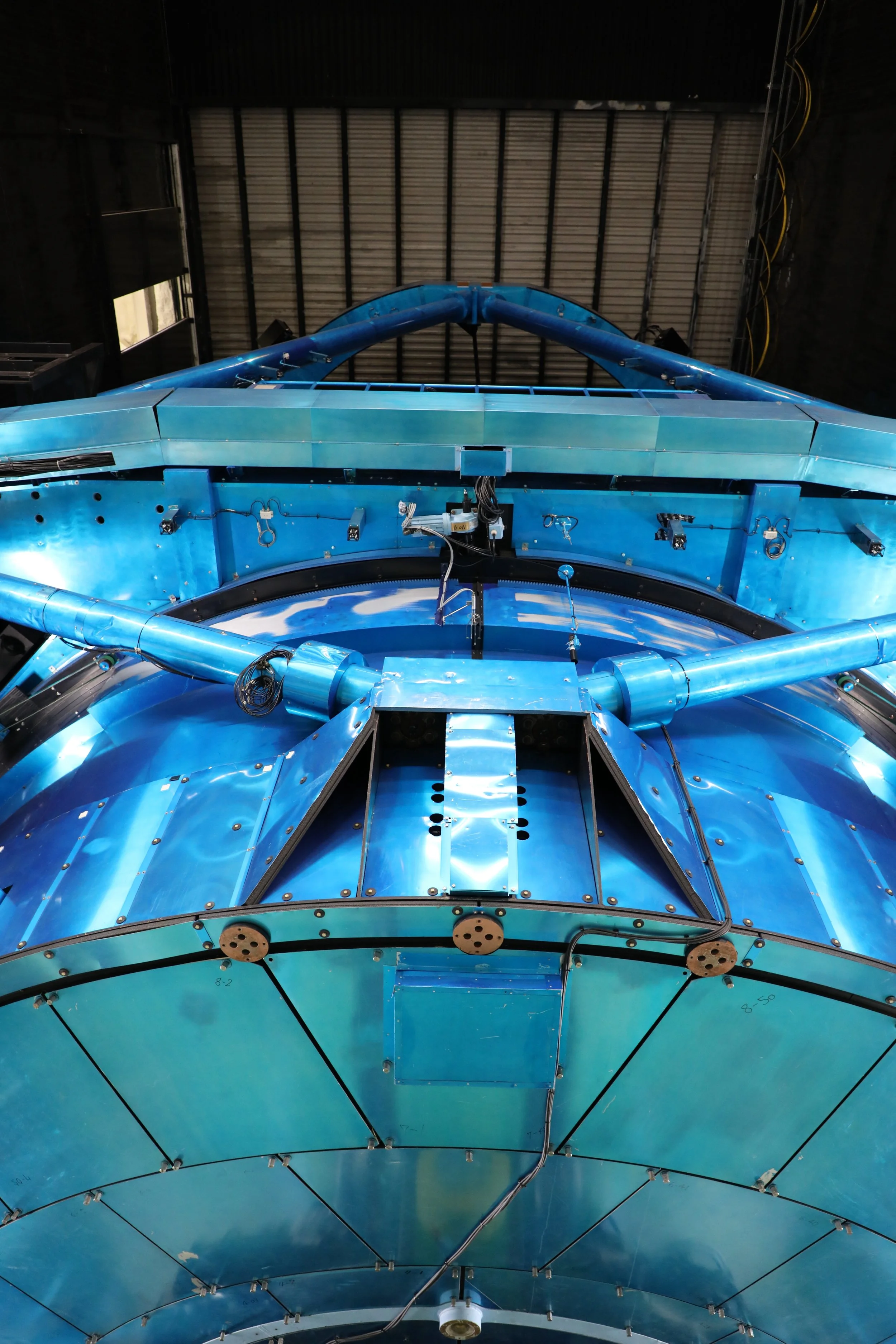A large blue structure or machine inside a warehouse or hangar, with metal panels, pipes, and electrical wiring.
